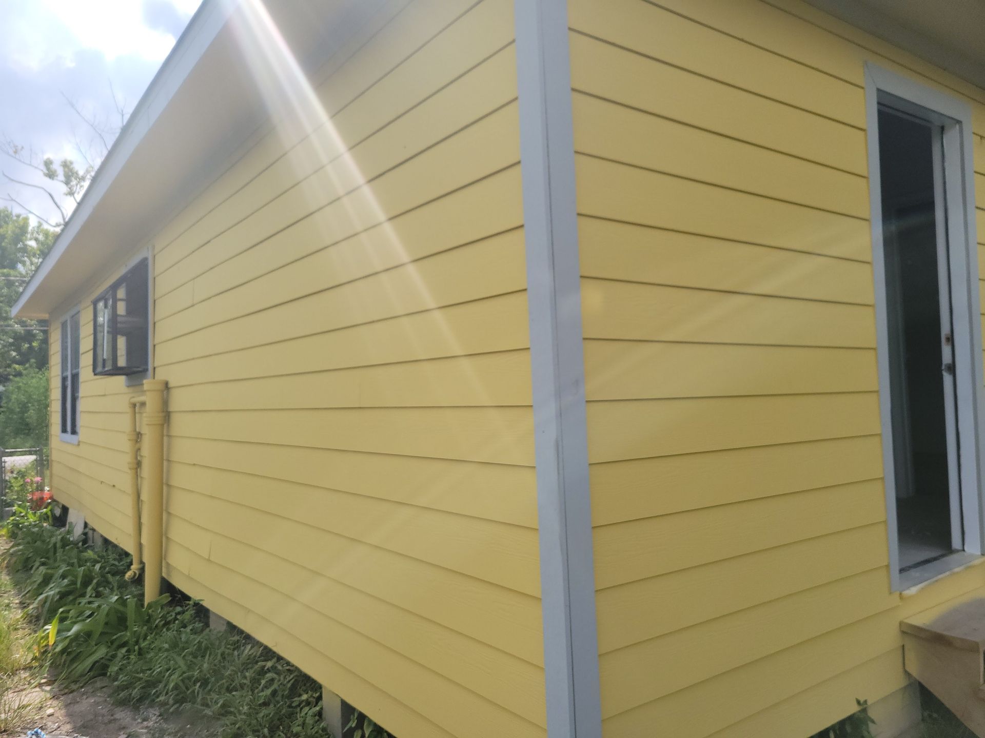 Yellow house with gray trim, two windows, and an open doorway.