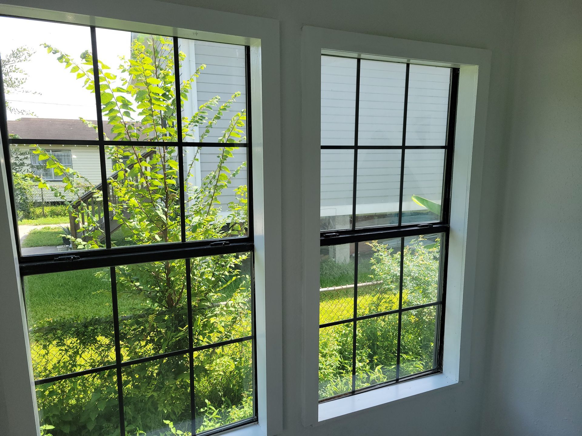 Two white-framed windows with black grids; greenery is visible through the glass.
