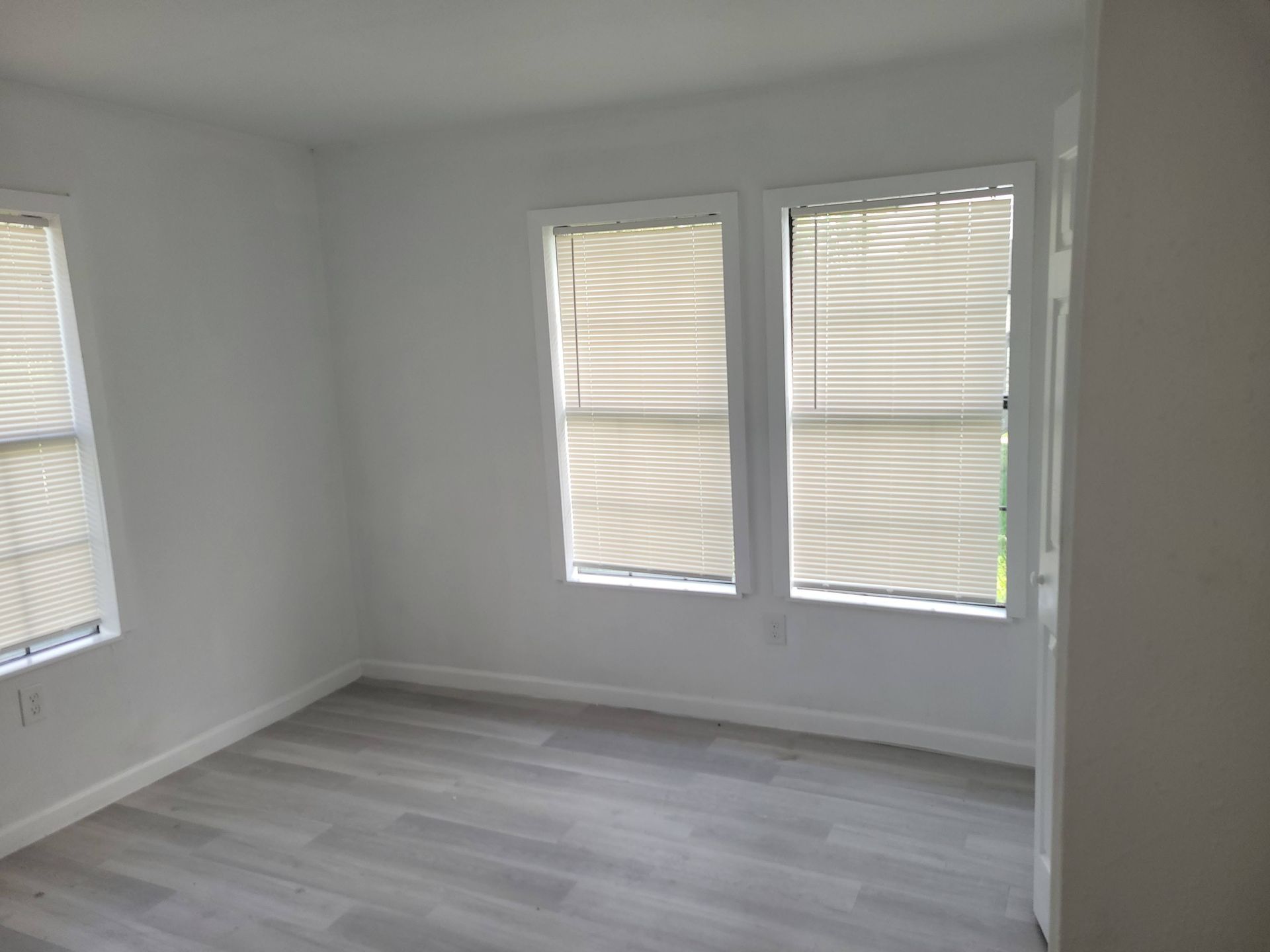 Empty room with two windows and blinds, light gray flooring, white walls.