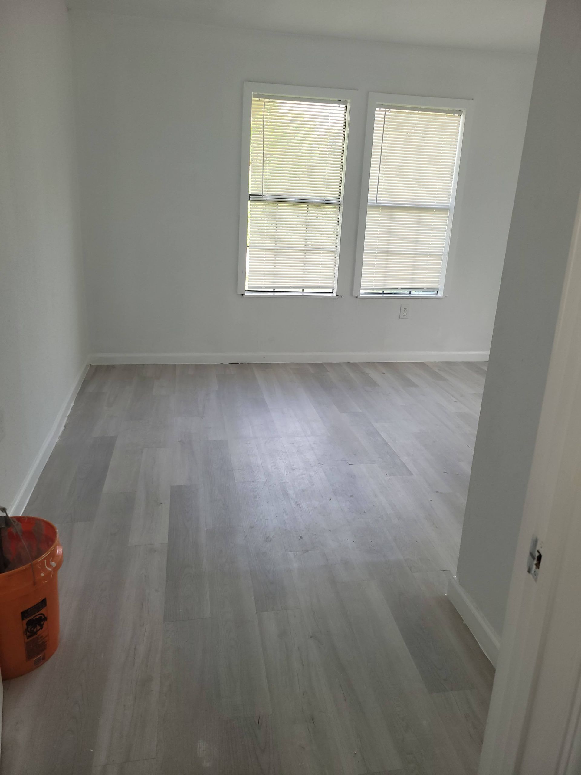 Empty room with grey flooring, white walls, and a window with closed blinds.
