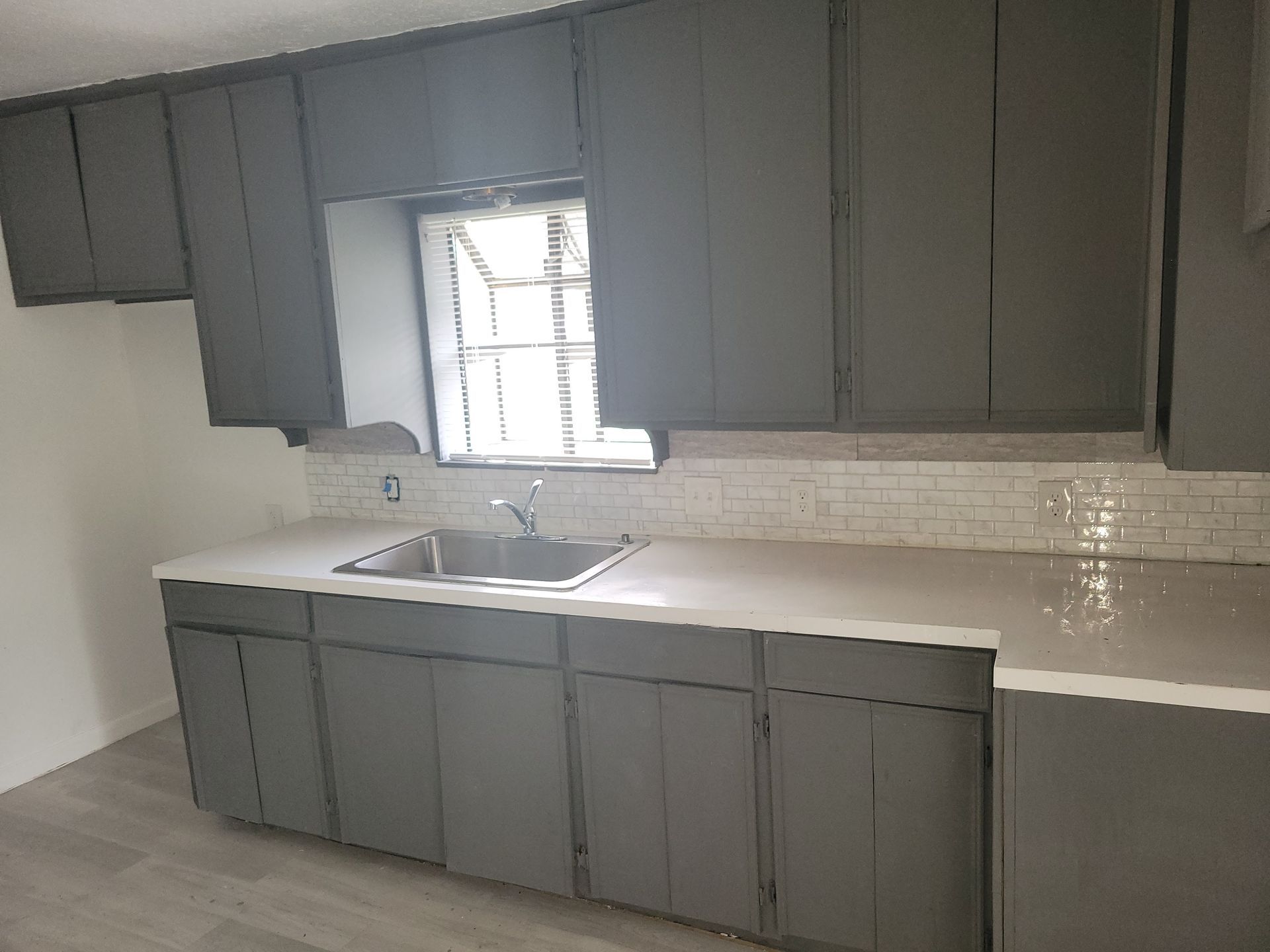 Gray kitchen cabinets with a white countertop and a window above the sink.