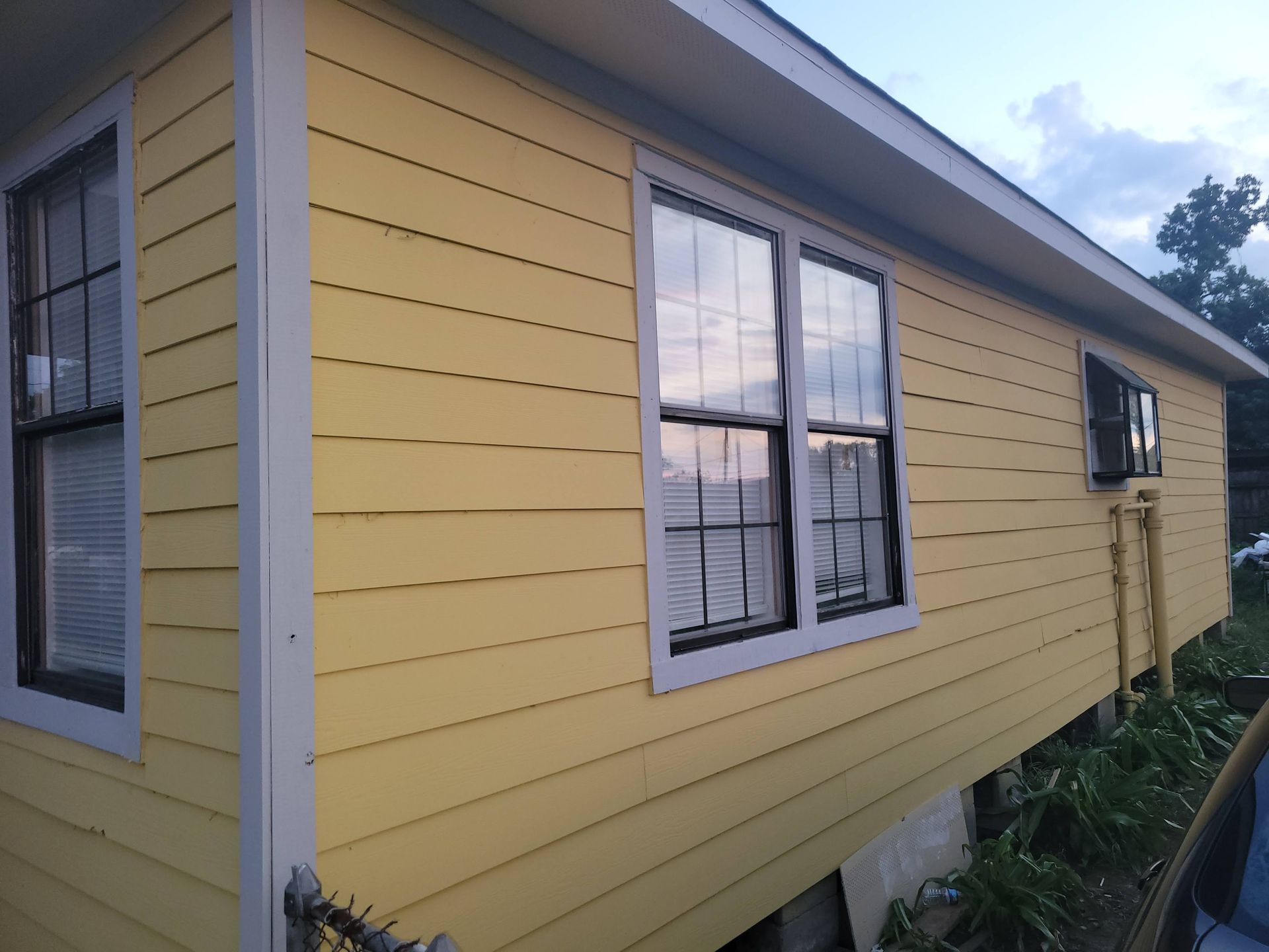 Yellow house with white trim and multiple windows, viewed from a low angle.