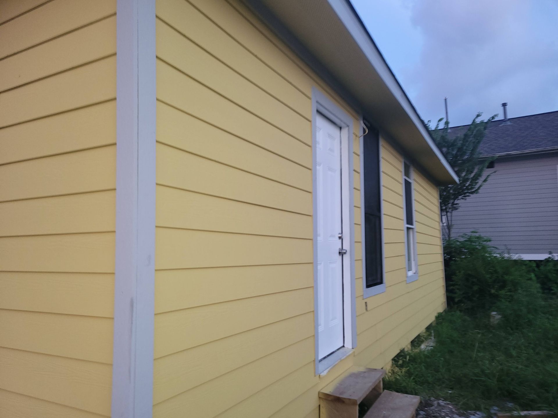 Yellow house with white door, black shutters, and tan trim.
