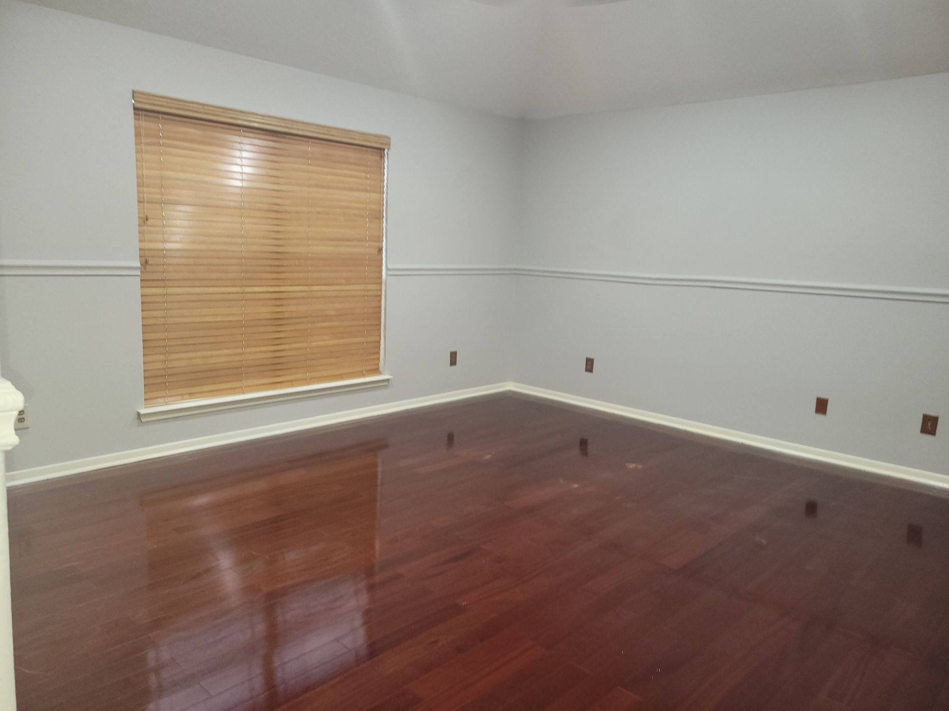 Empty room with dark hardwood floors, light gray walls, and a wooden blind on the window.