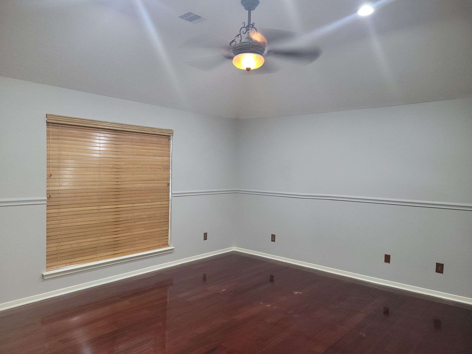 Empty room with wooden blinds, hardwood floor, and ceiling fan. Gray walls, brown blinds.