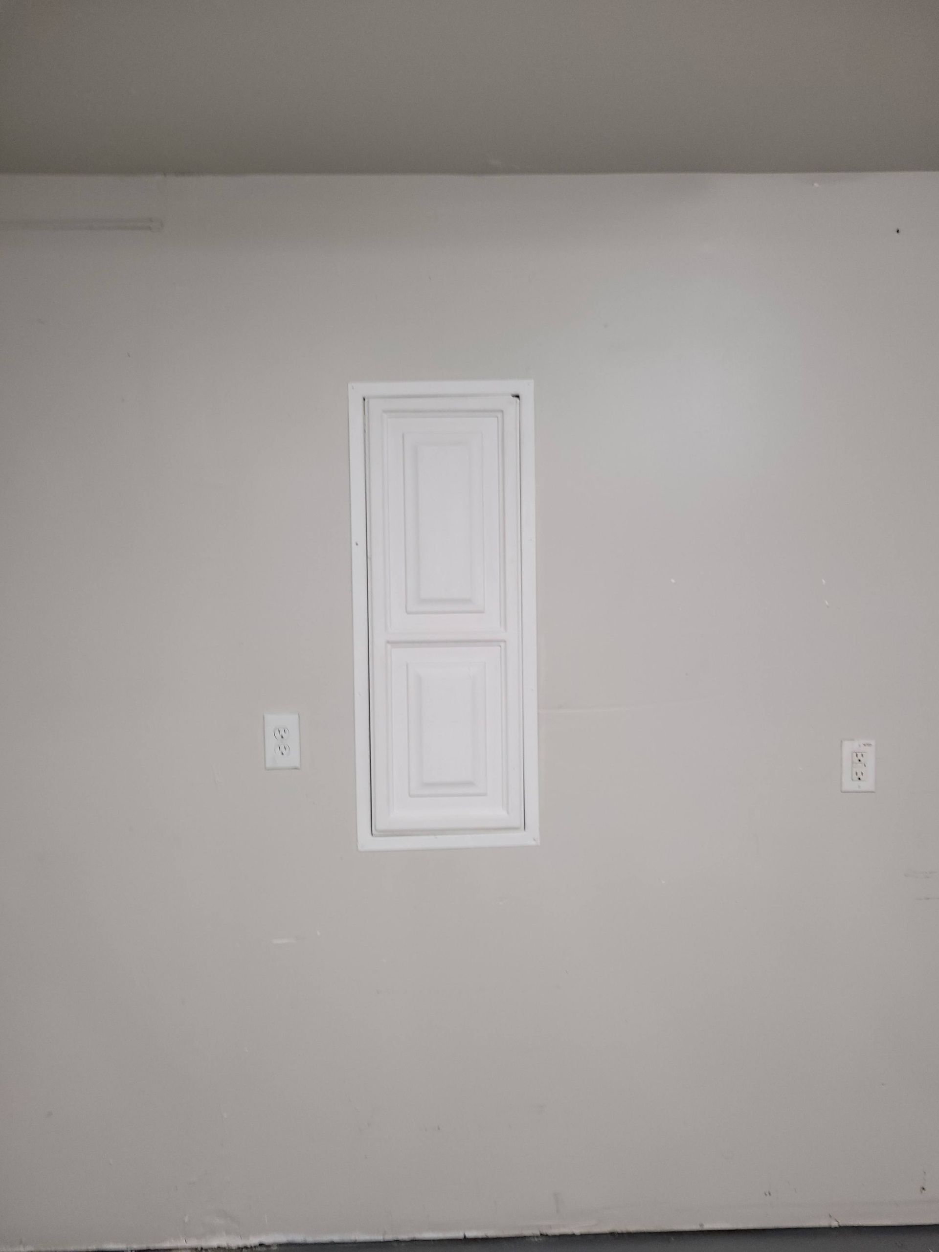 Gray wall with a recessed, white cabinet centered between two electrical outlets.