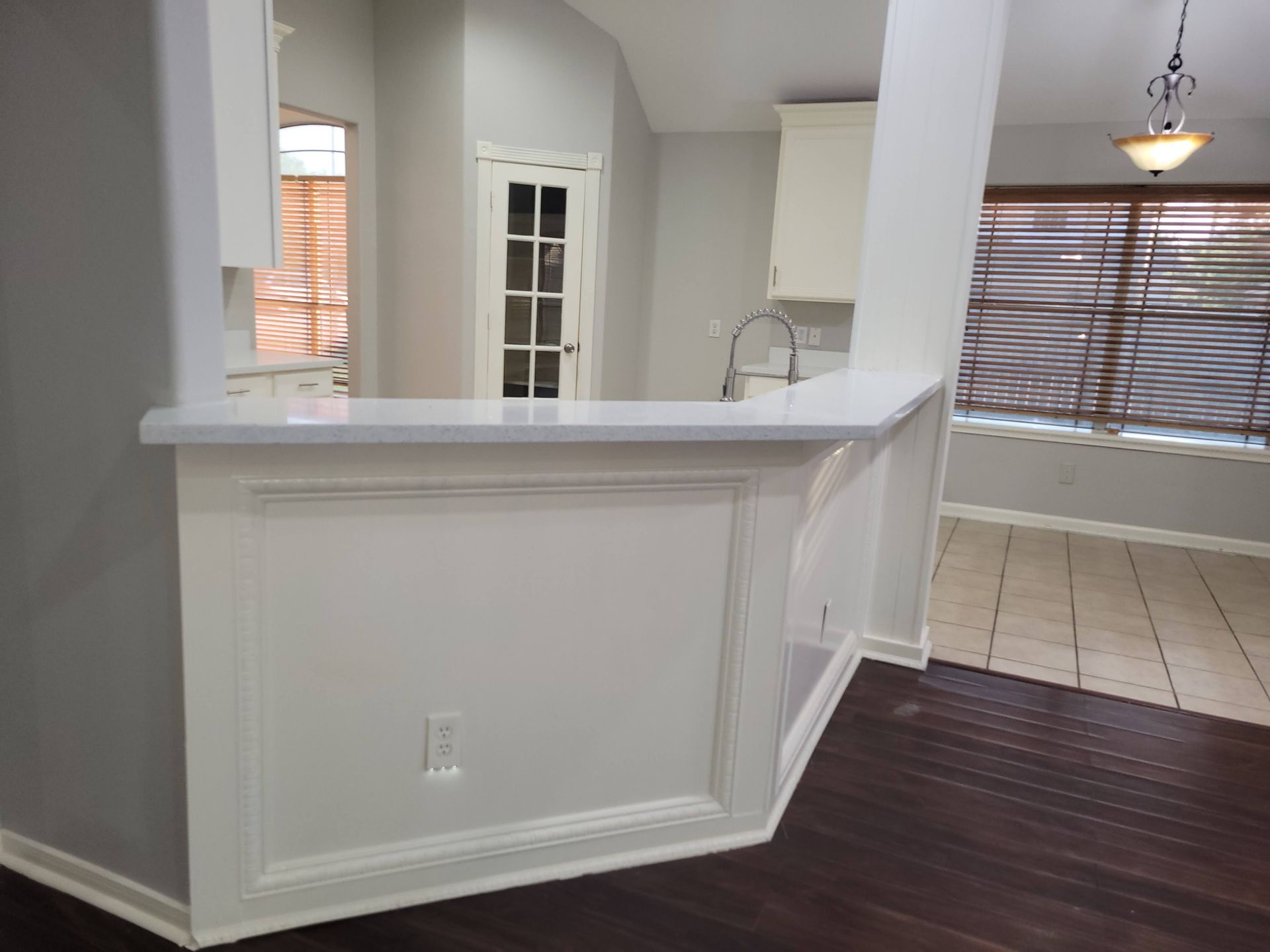 Interior view with a white countertop and trim, leading to a kitchen and dining area with dark wood flooring.