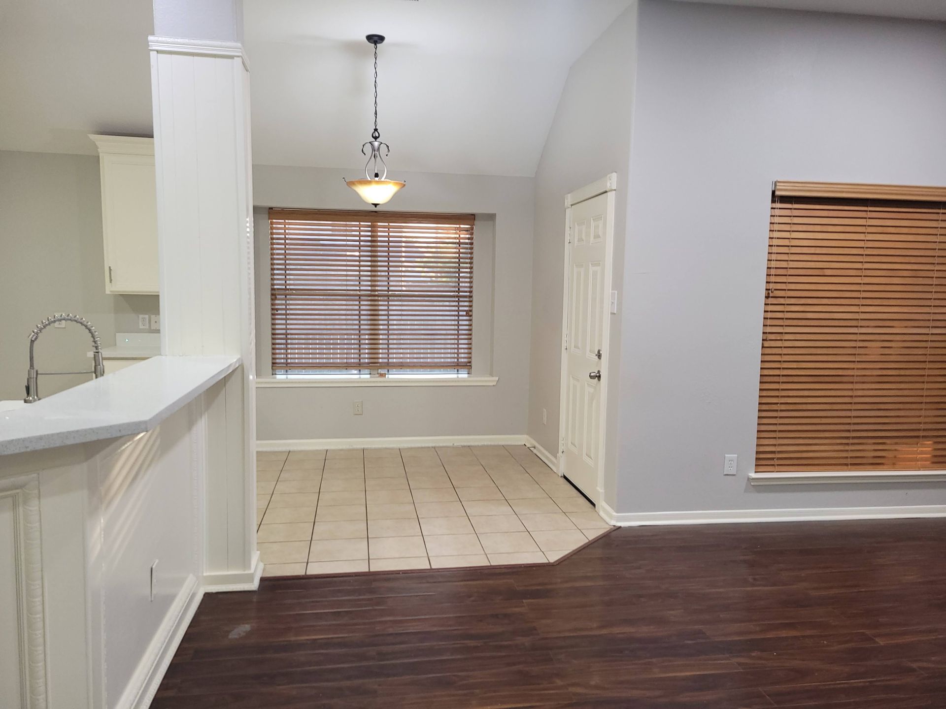 Interior view of a dining area with tile floor, dark wood-look floor, light gray walls, and window blinds.