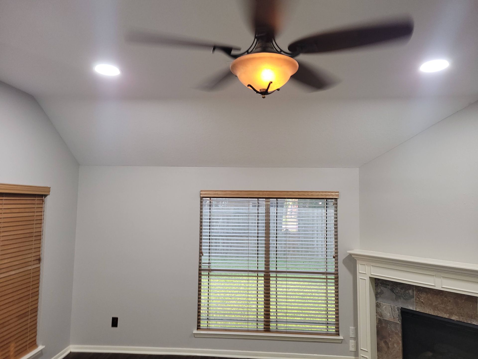 Living room with a ceiling fan, recessed lights, window with blinds, and a fireplace.