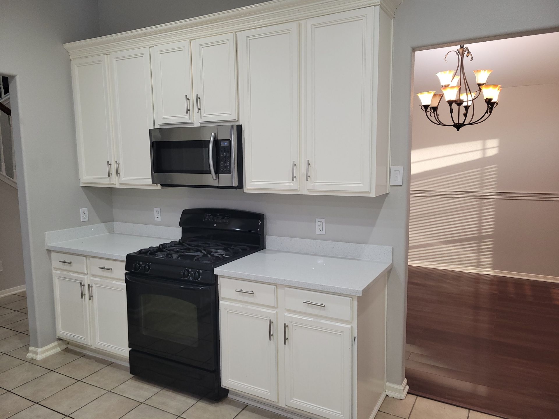 White kitchen cabinets with a black stove and microwave, open doorway to dining area.
