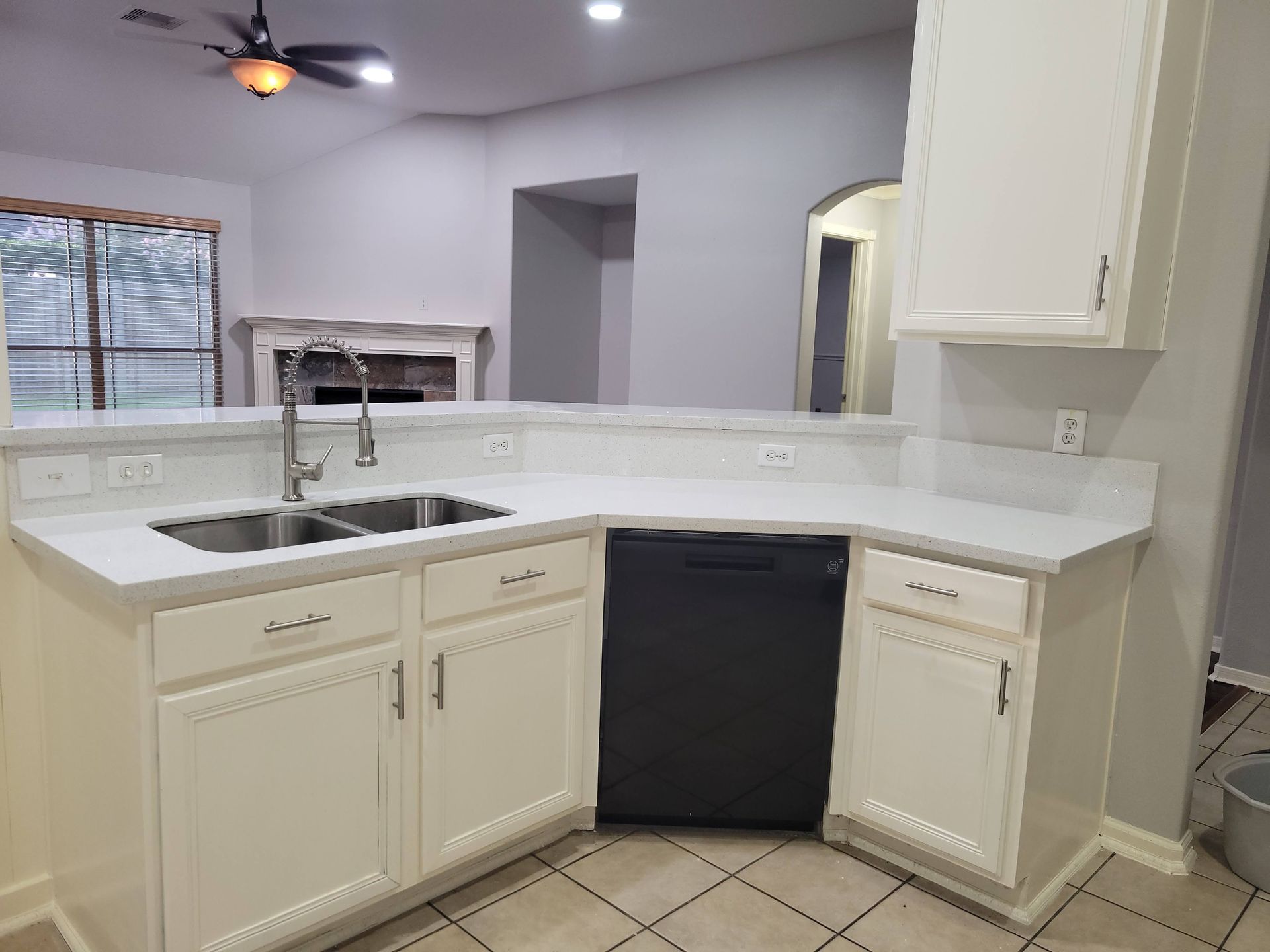 White kitchen with countertops, sink, cabinets, dishwasher, and open view to living area with fireplace.