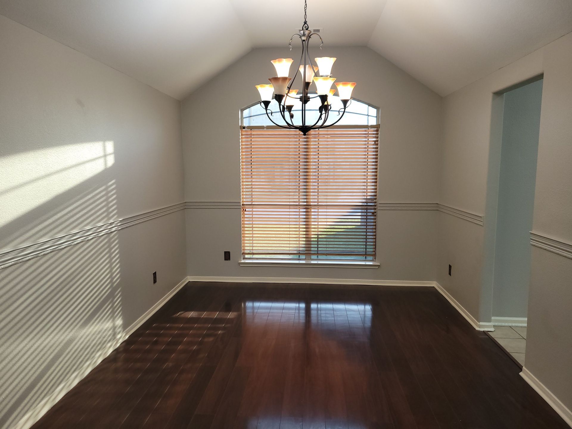 Dining room with dark wood floor, arched window with blinds, and chandelier.