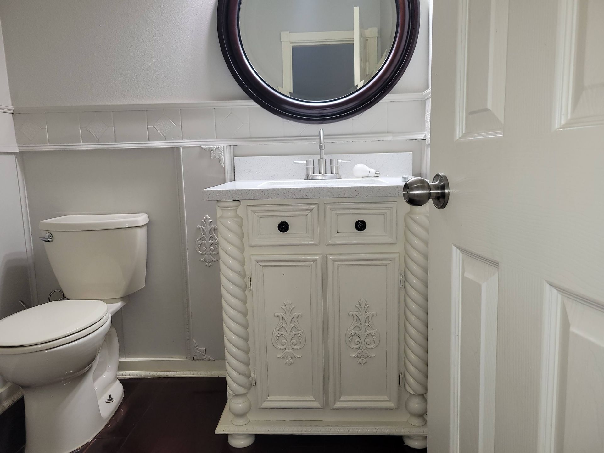 Bathroom with white vanity, toilet, and a round mirror.