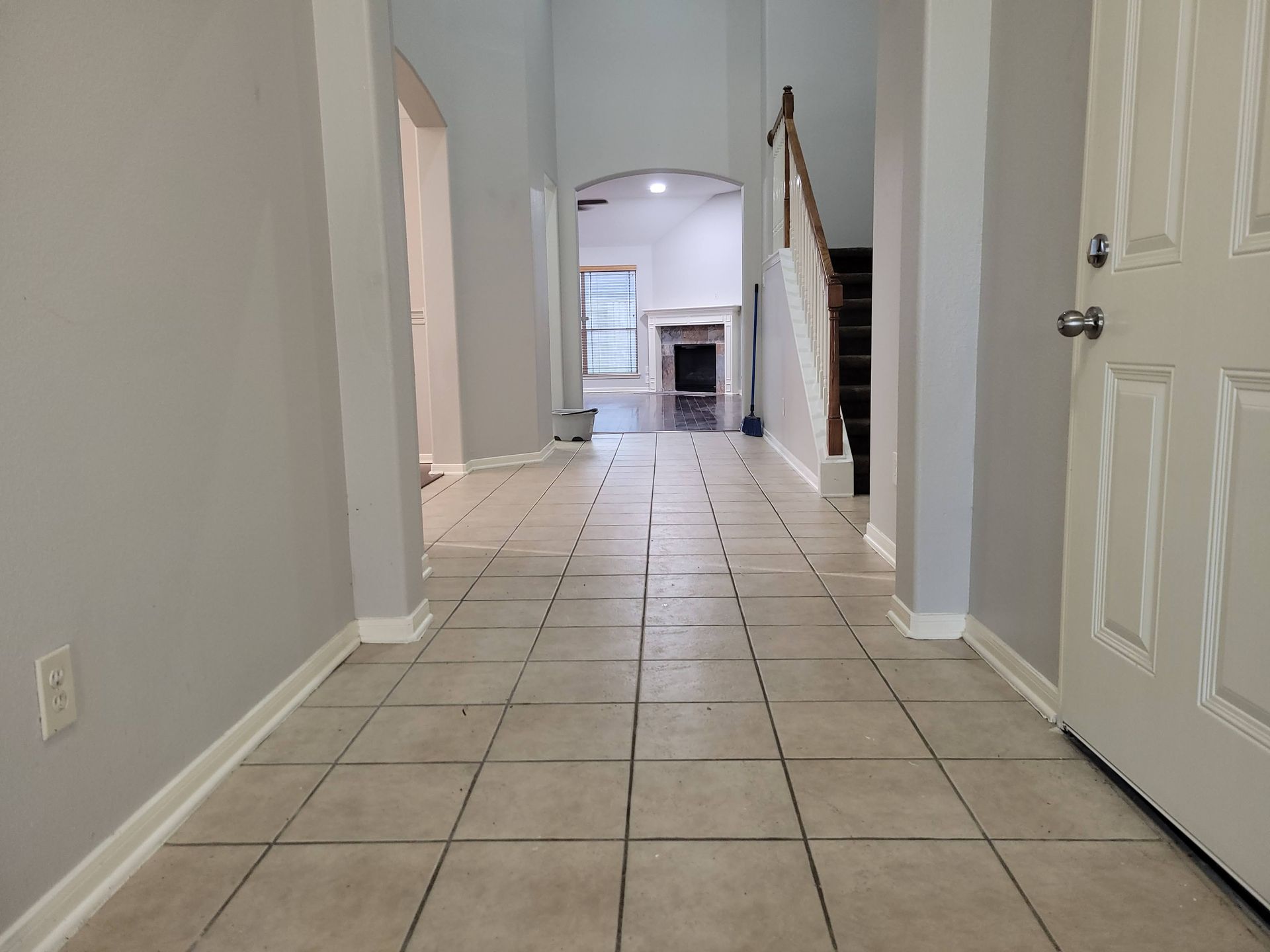 Entryway with tiled floor, gray walls, and staircase. Door on the right and opening to another room in the distance.