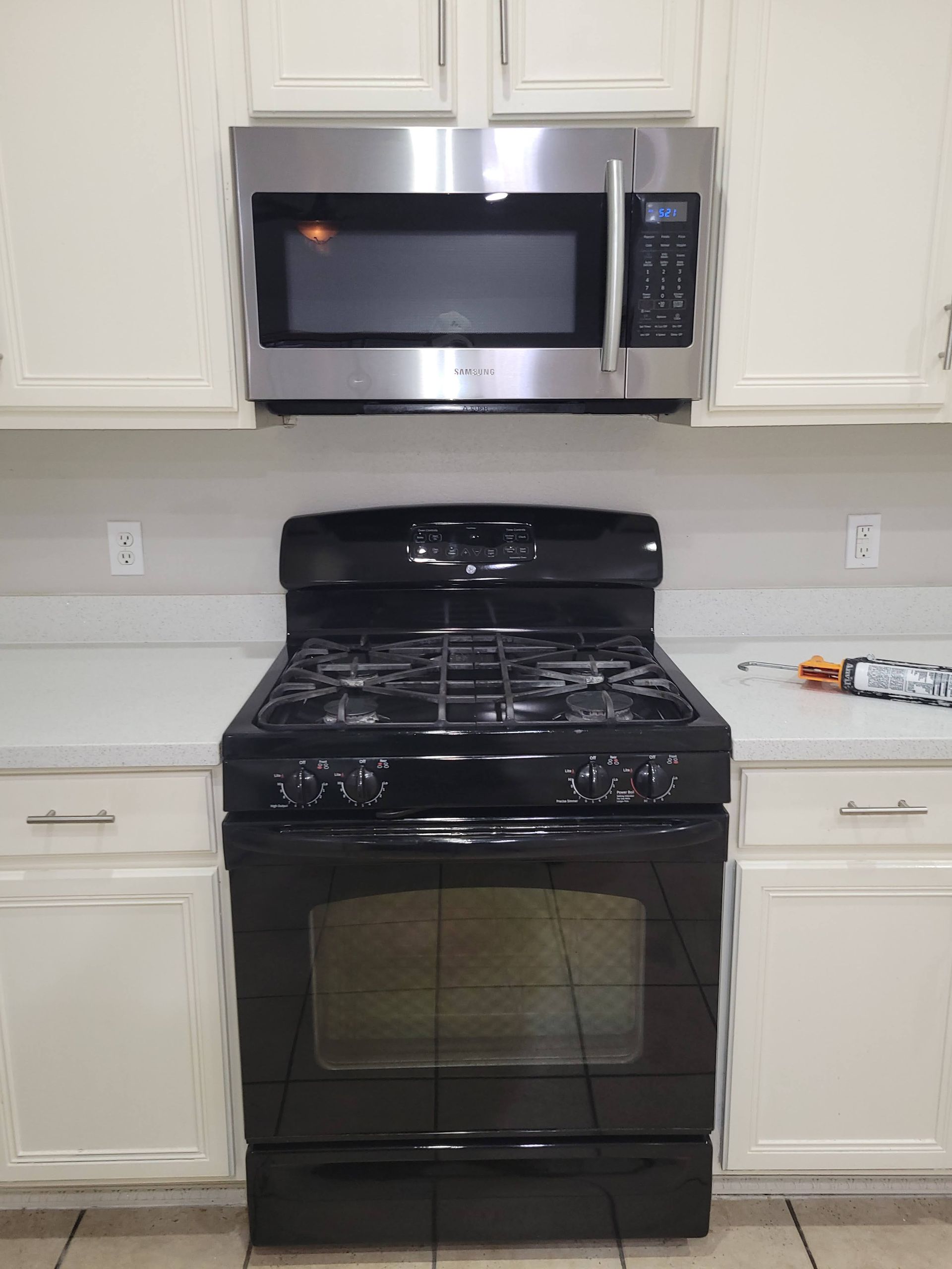 Black gas range and stainless steel microwave in a kitchen. White cabinets.