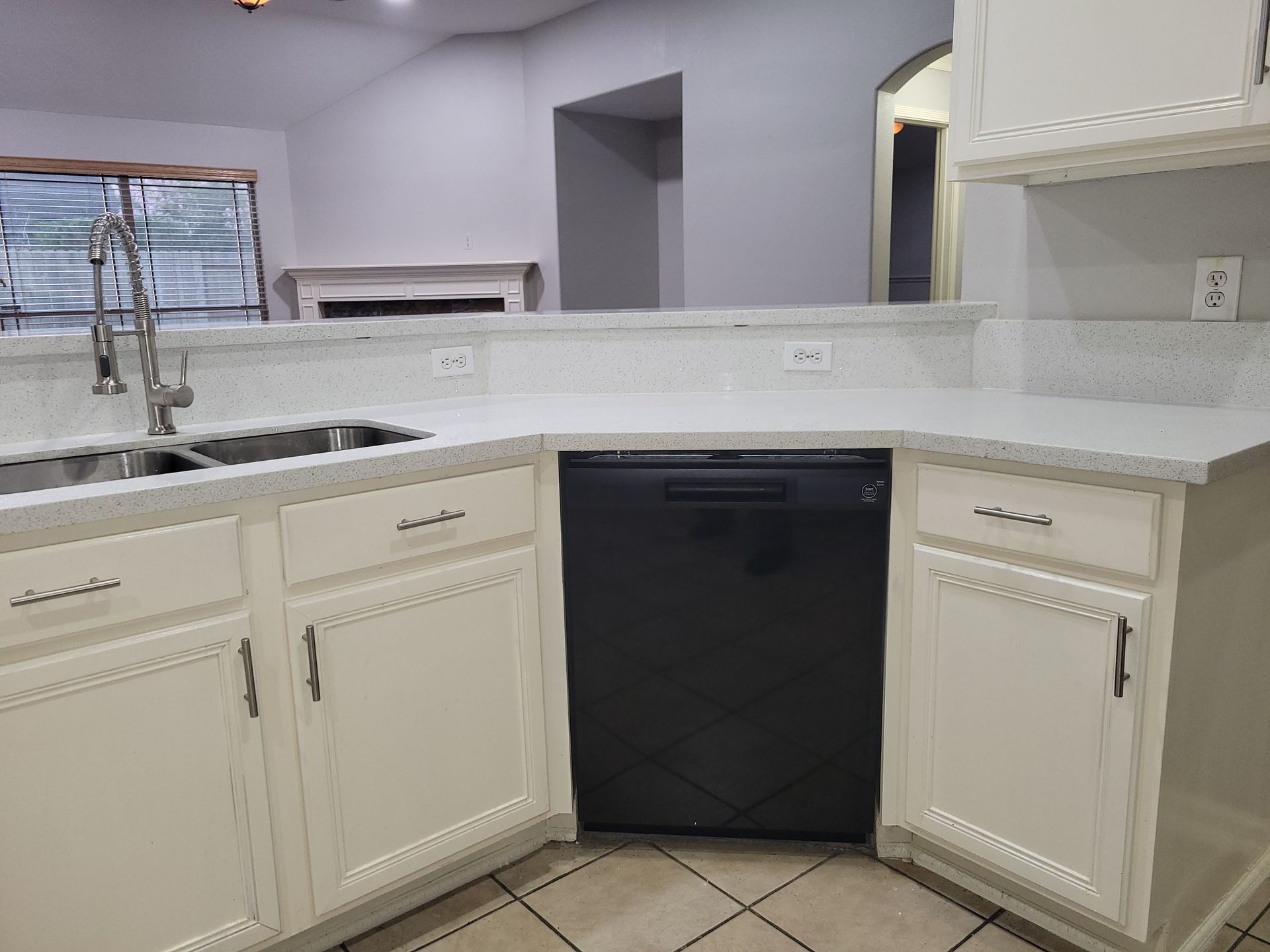 White kitchen cabinets with black dishwasher and silver faucet, white countertops.