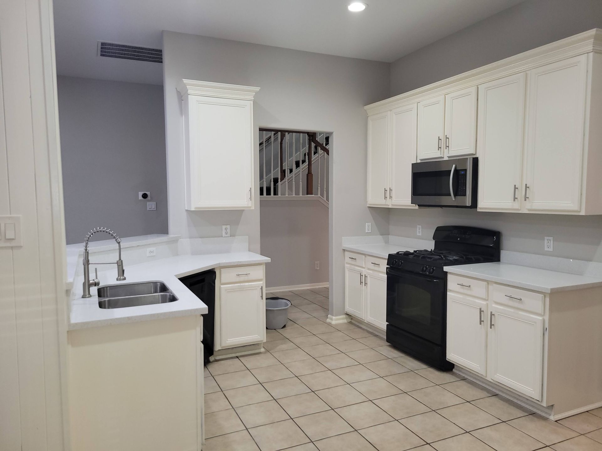 White kitchen with cabinets, stove, sink, and countertops; a staircase is visible through a window.