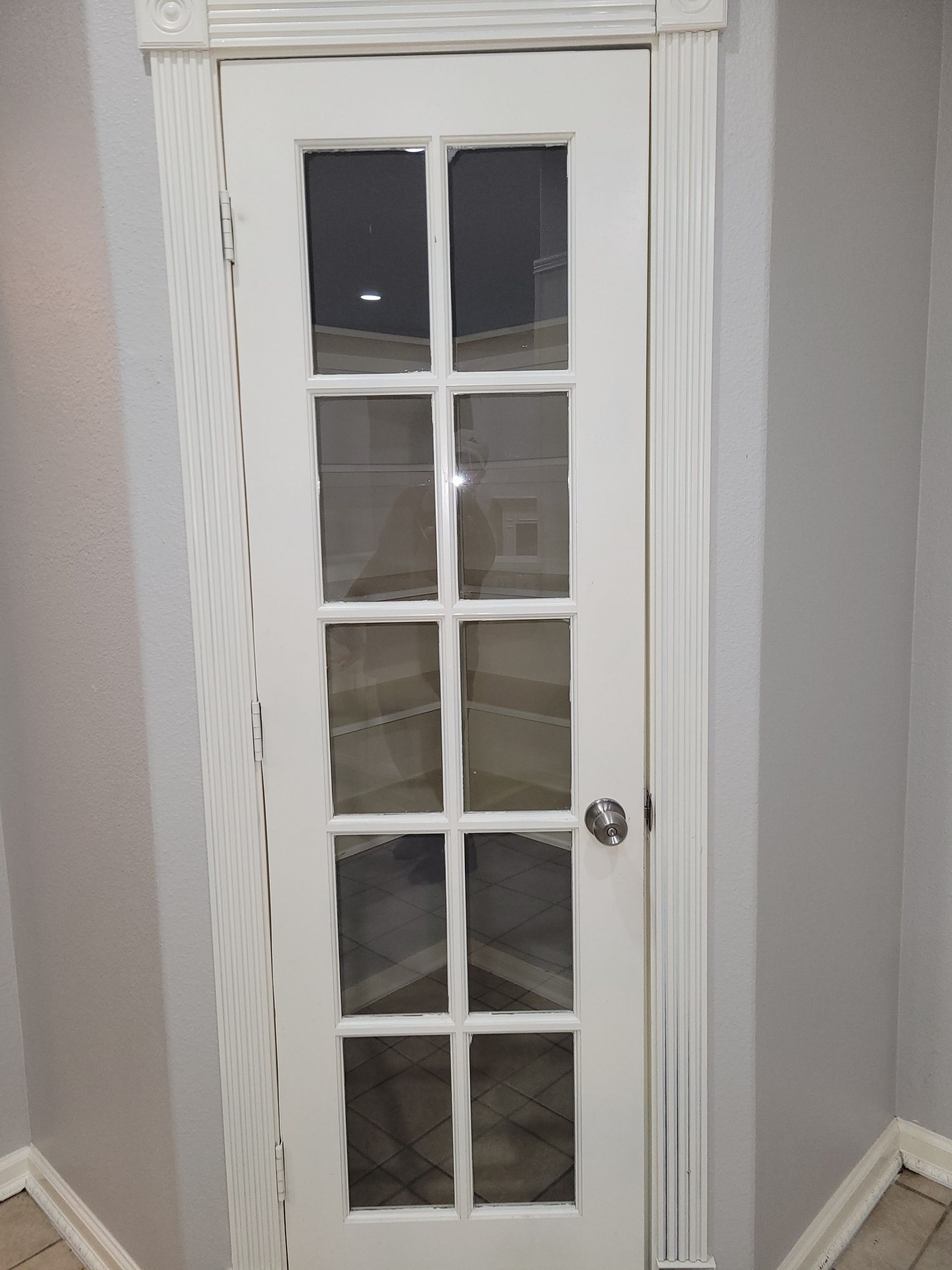 White glass-paneled door with ornate trim in a corner of gray-painted room.