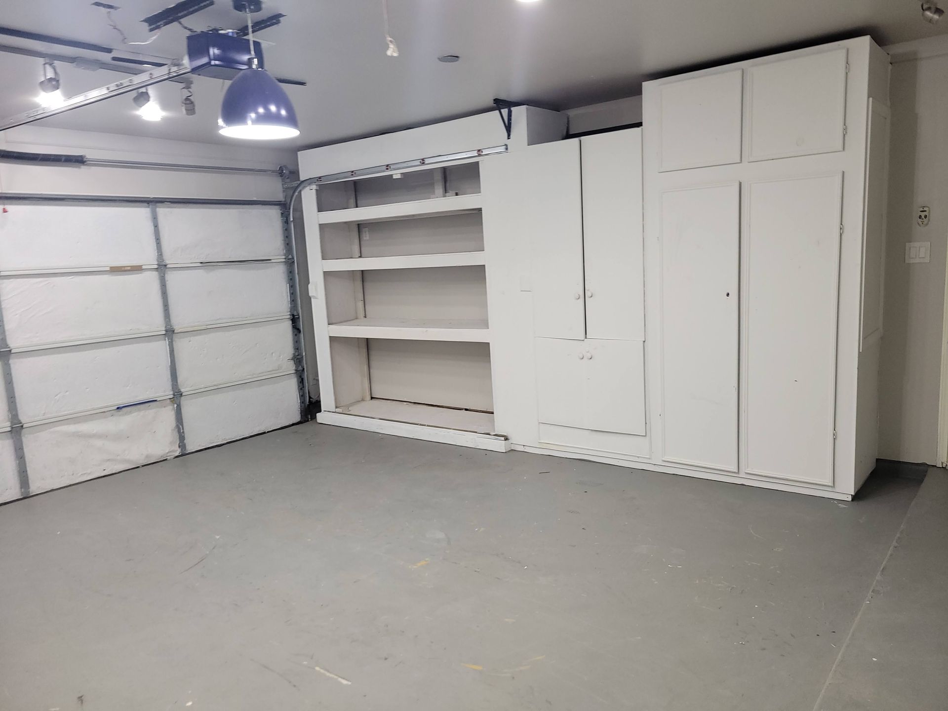Garage interior with white cabinets and shelving on a gray painted floor. Garage door closed on the left.