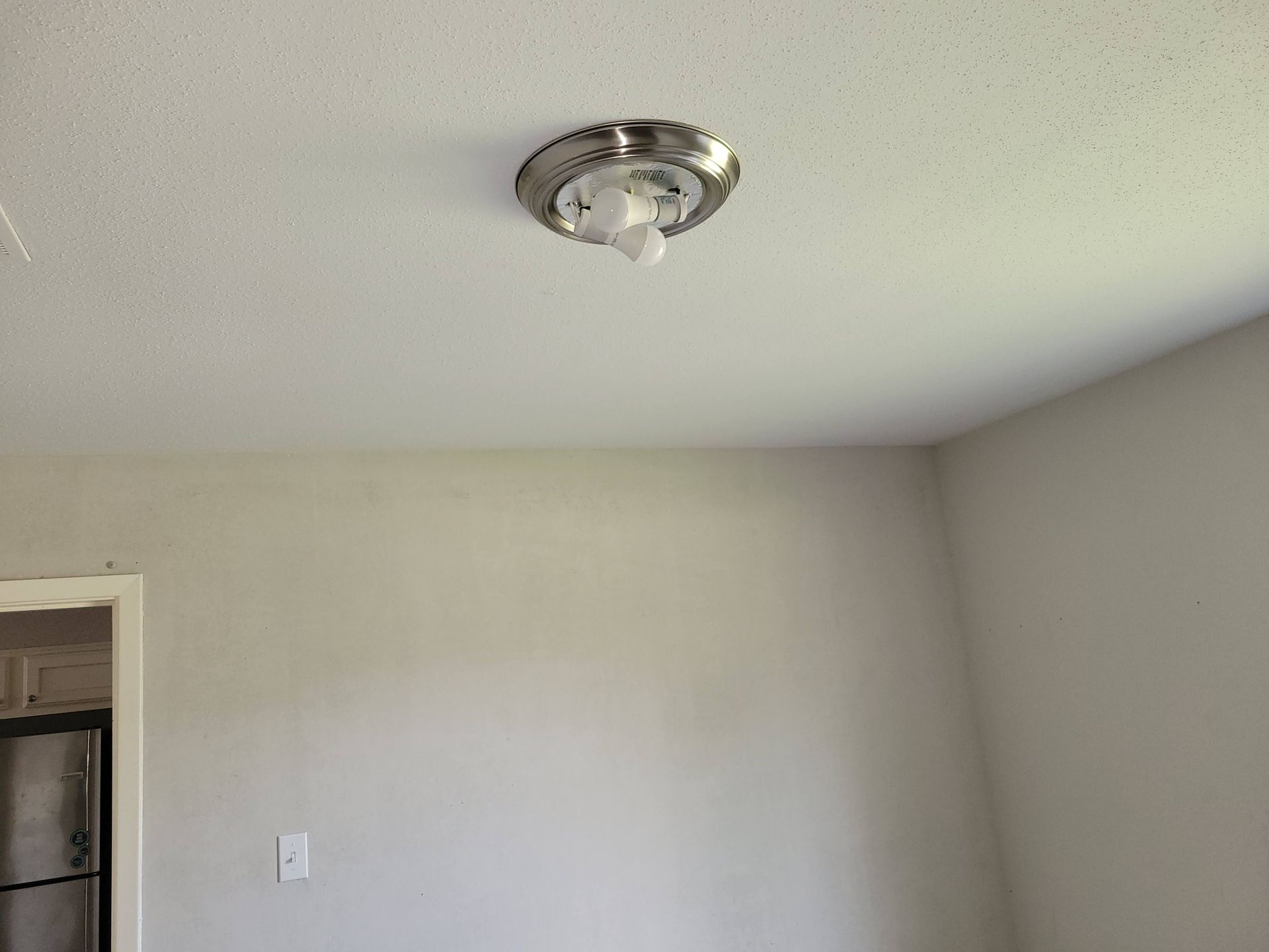 Ceiling light fixture with broken globe on a white ceiling in a room with light gray walls.