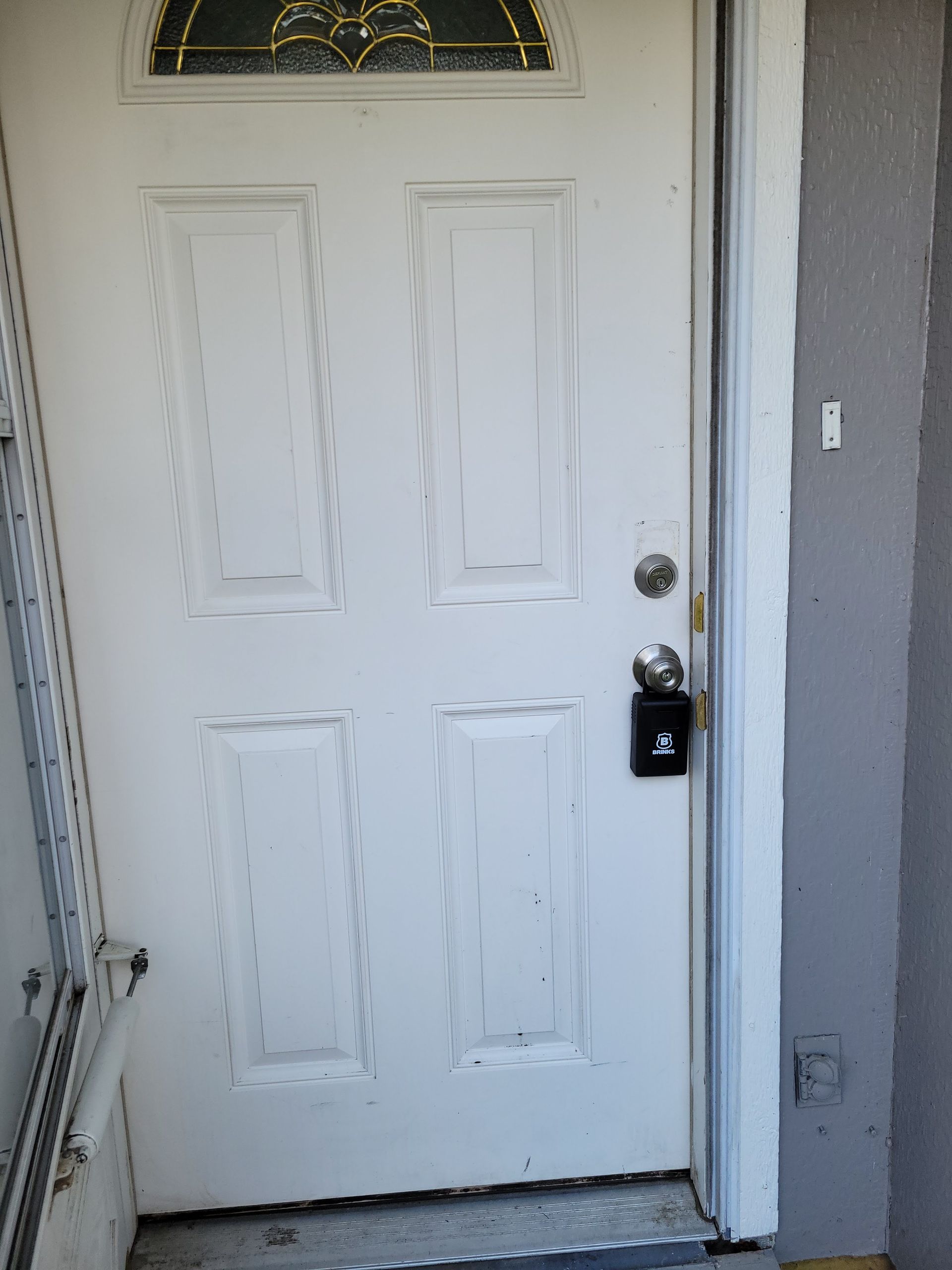 White exterior door with a window at the top, a lock, and a keypad lock; in a gray wall setting.