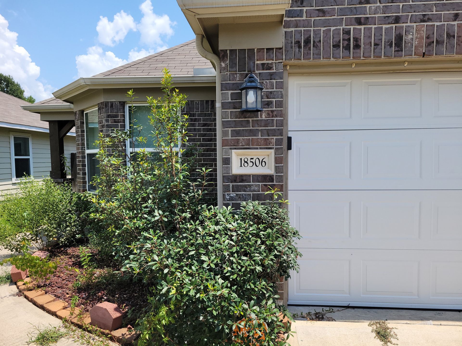 Exterior view of a house with a brown brick facade, white garage door, and address 18506.