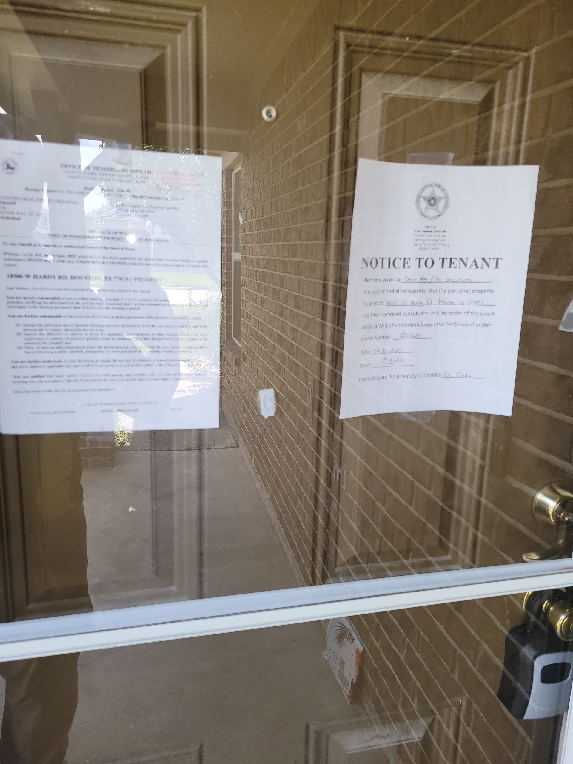 Closed glass door with eviction notices posted on it. Brick wall is visible behind the door.