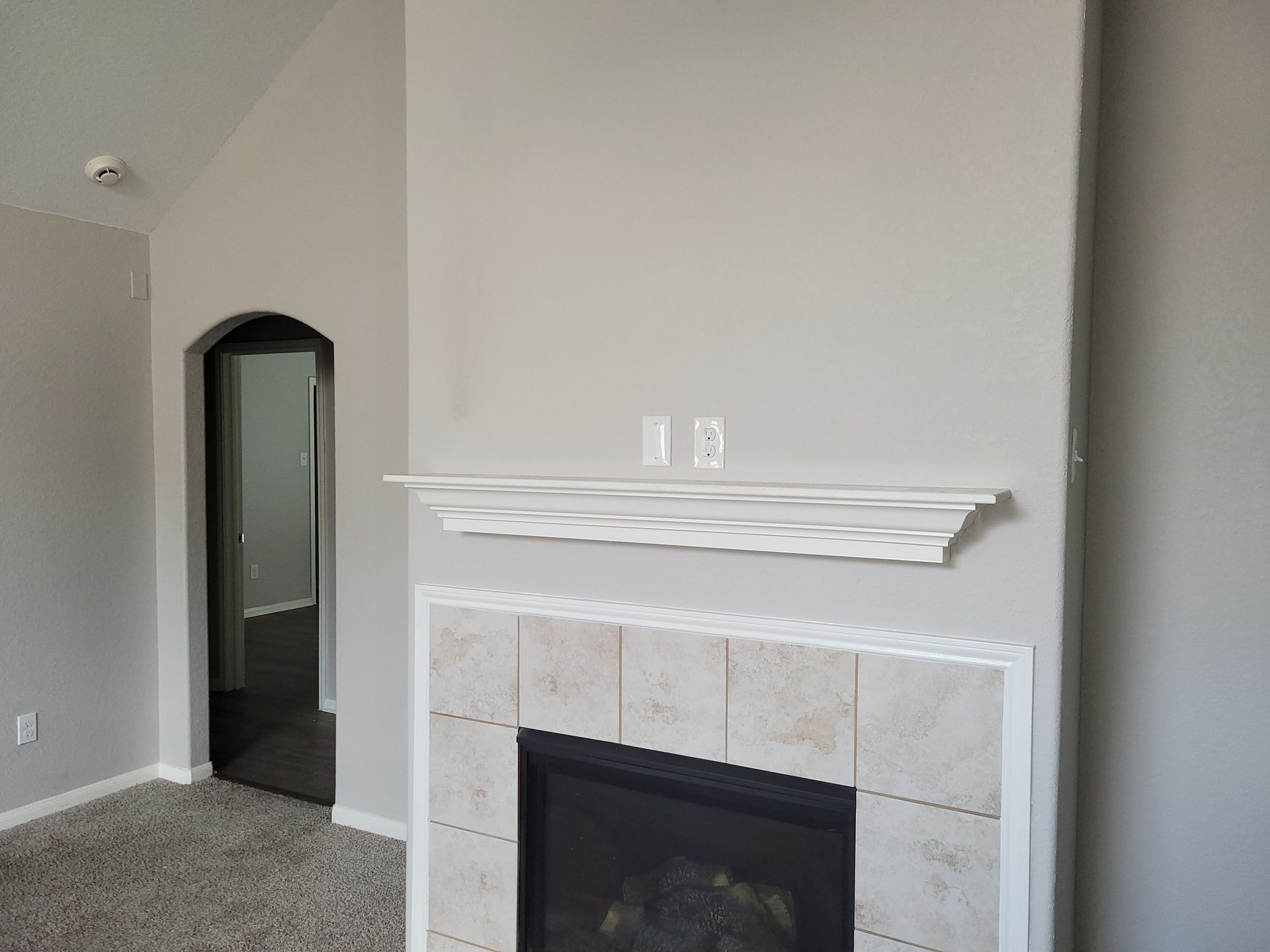 Fireplace with white mantel and tile surround, gray walls, and an arched doorway.
