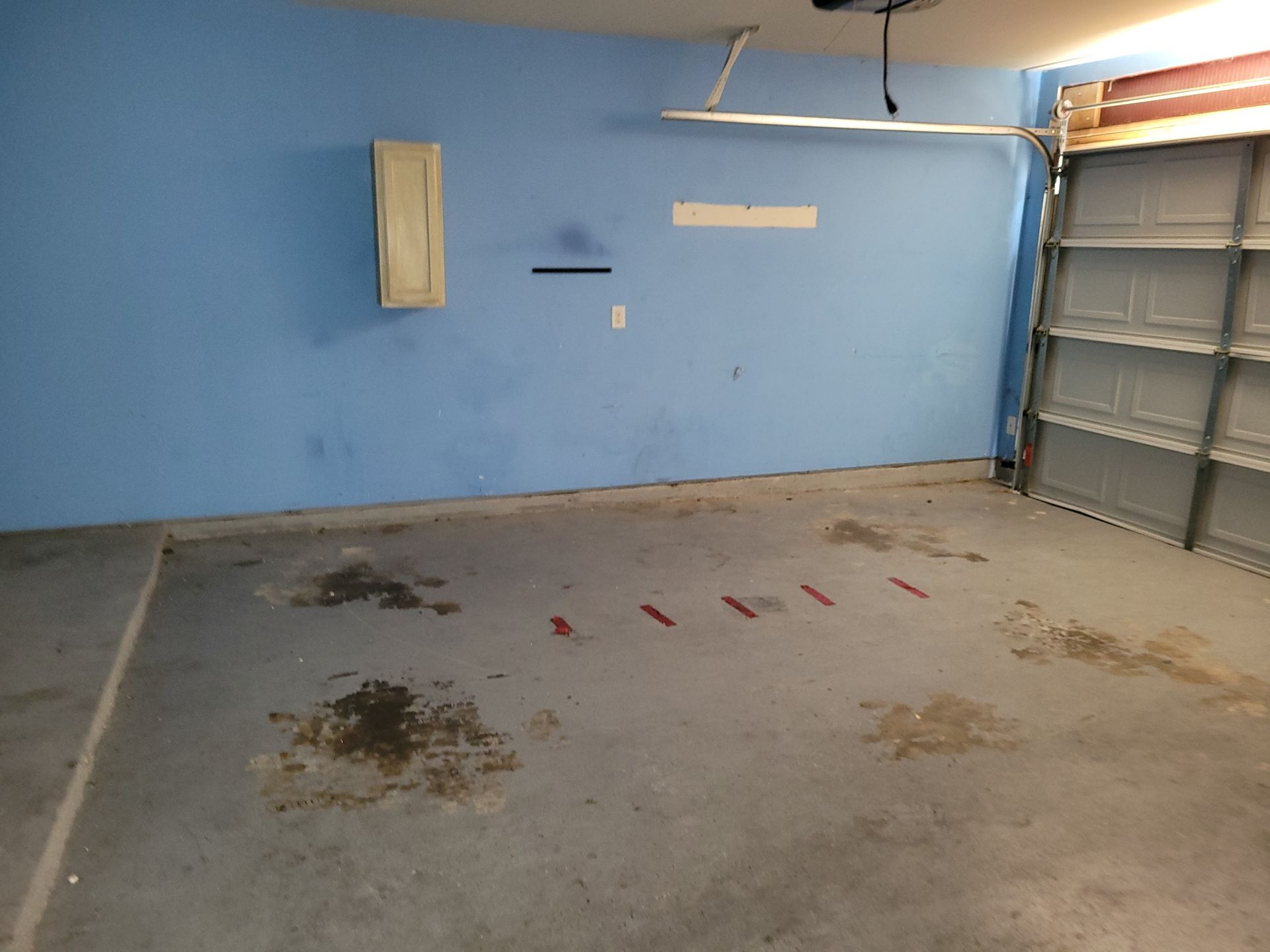 Blue-walled garage with concrete floor. Dark stains on floor, garage door open to the right.