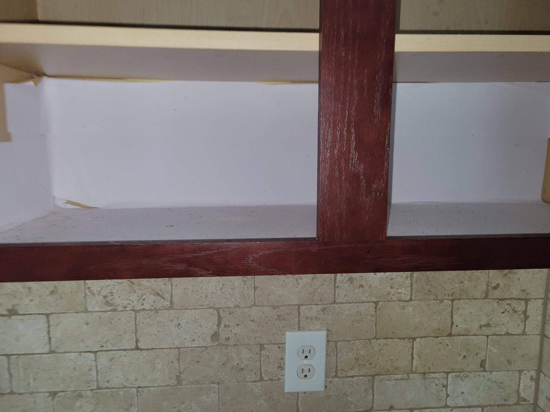 Built-in shelves with a burgundy-colored support beam. White painted interior with beige brick backsplash.