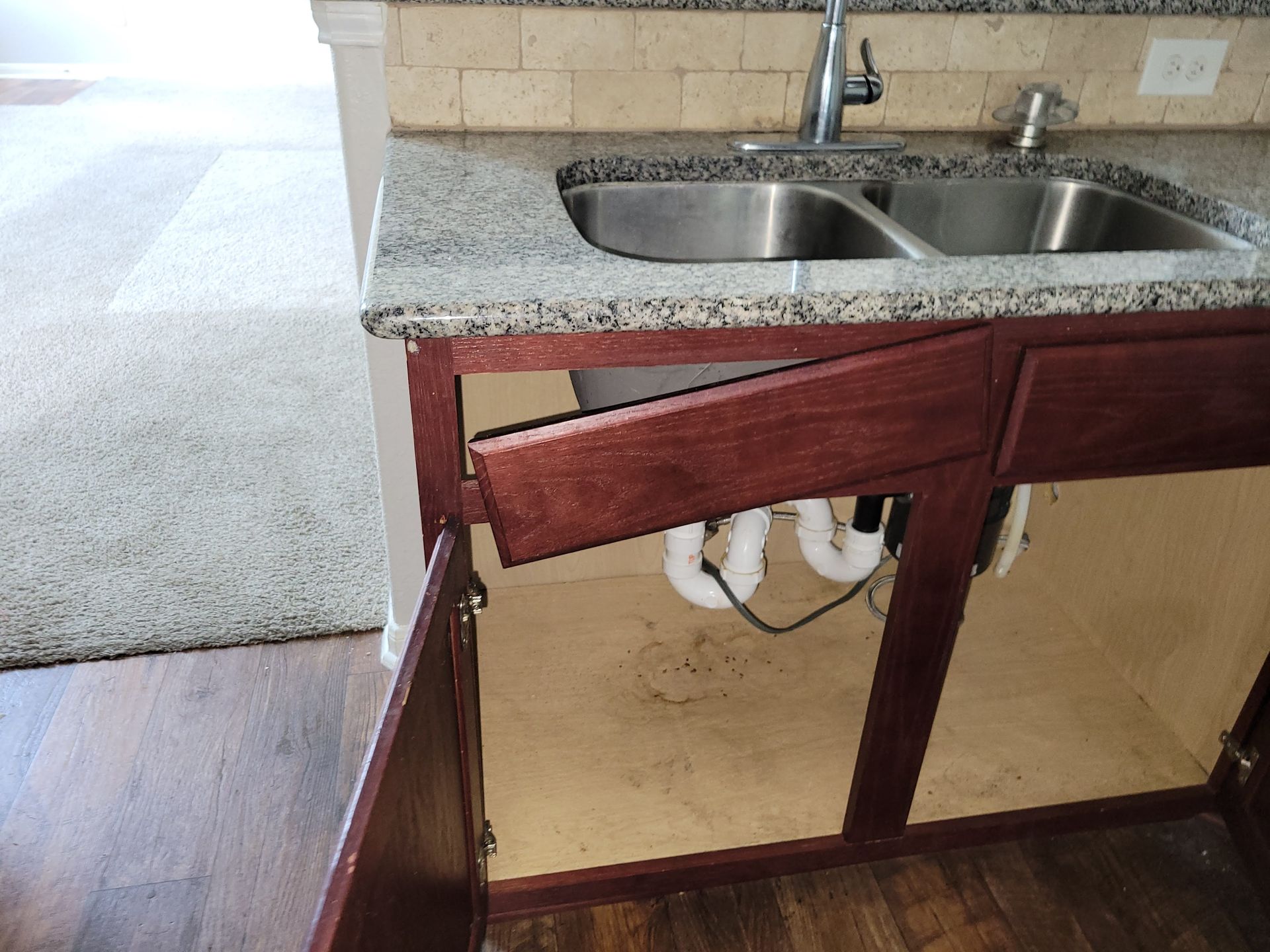Kitchen cabinet with a detached drawer and open doors under a sink.