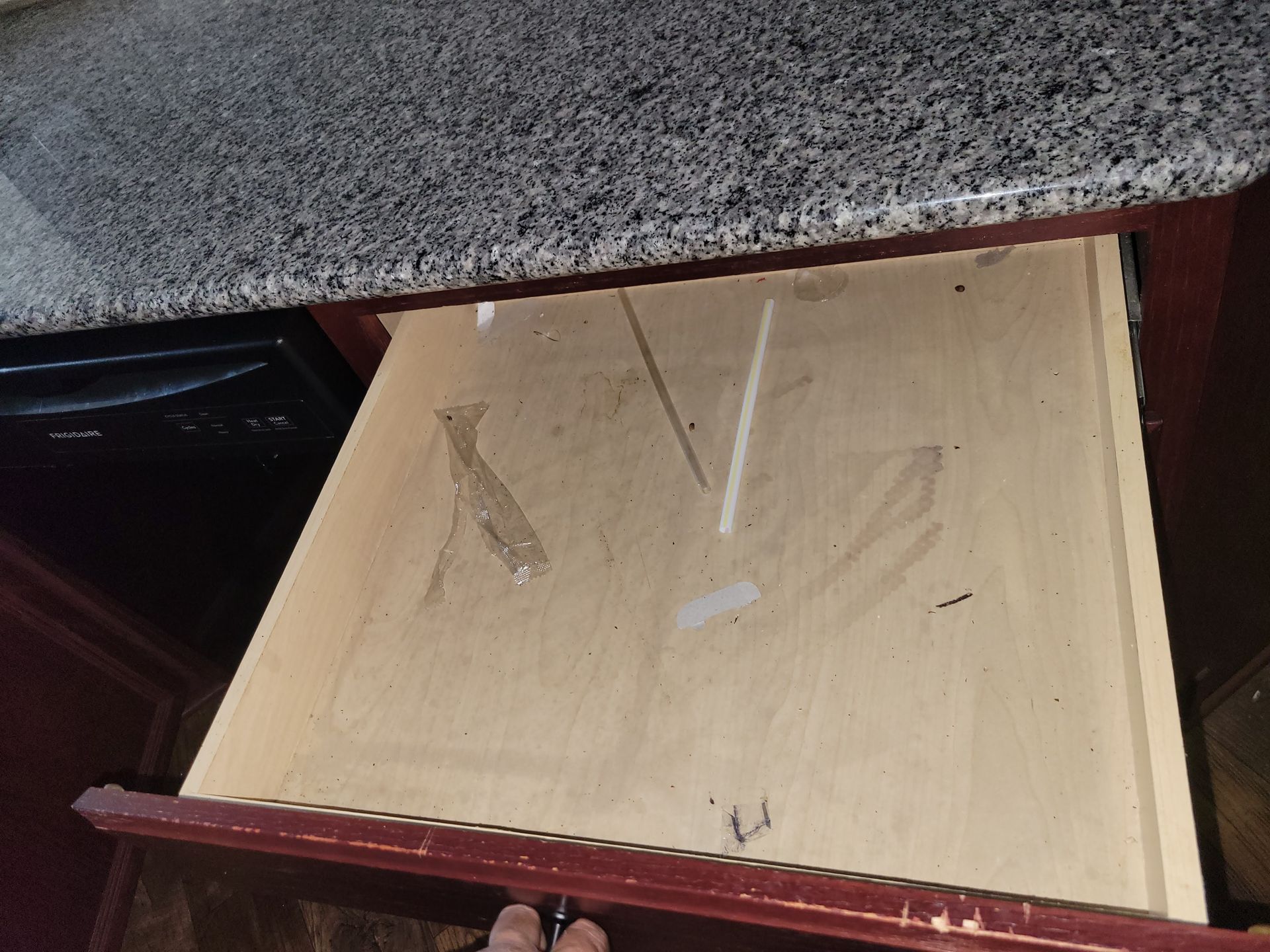 Open kitchen drawer under a granite countertop, showing interior wood and remnants of tape.
