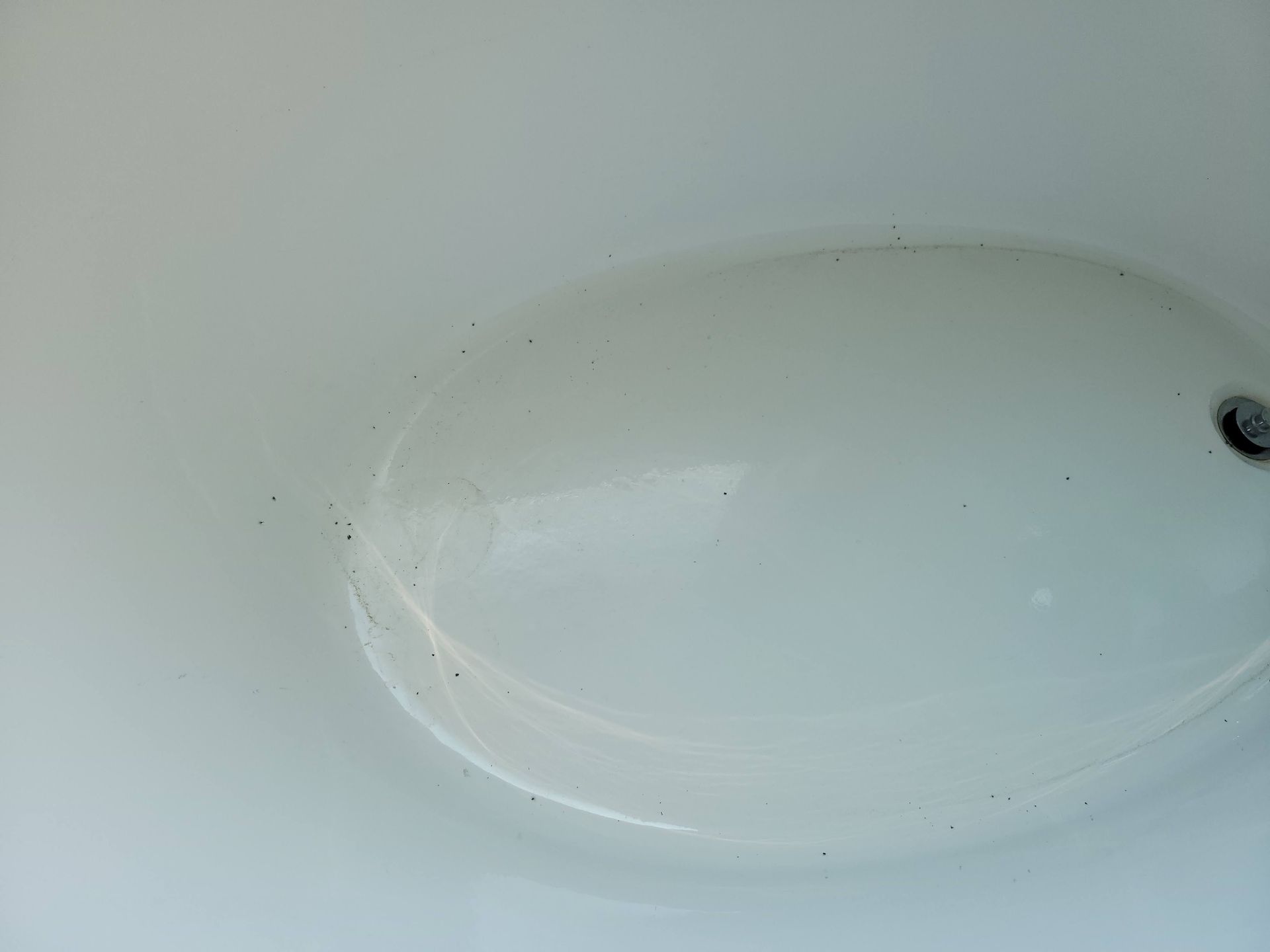 White porcelain sink with dark specks near the bowl's edge, drain visible.