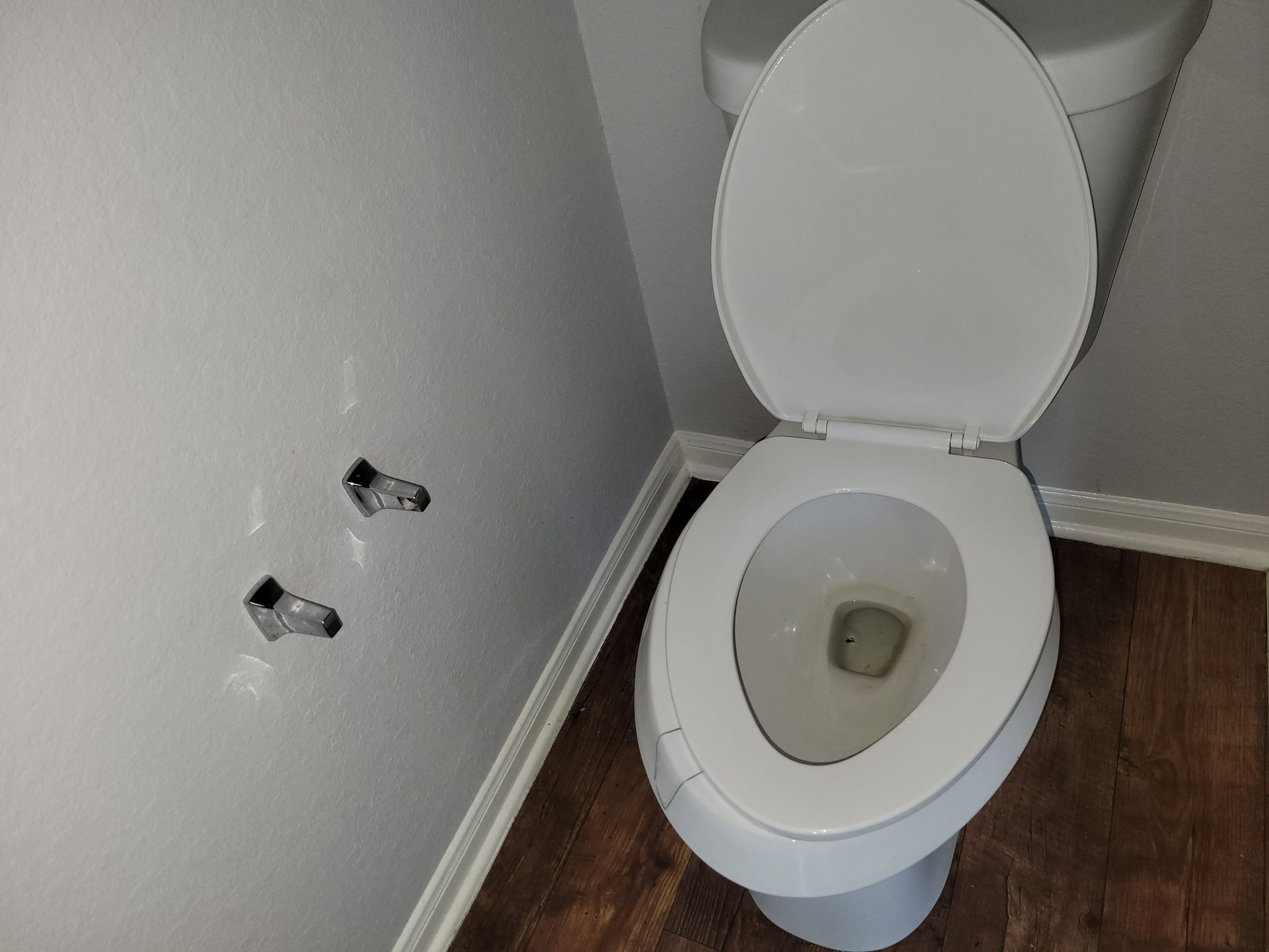 Toilet with open lid in a bathroom corner. Two wall fixtures are present near the toilet.