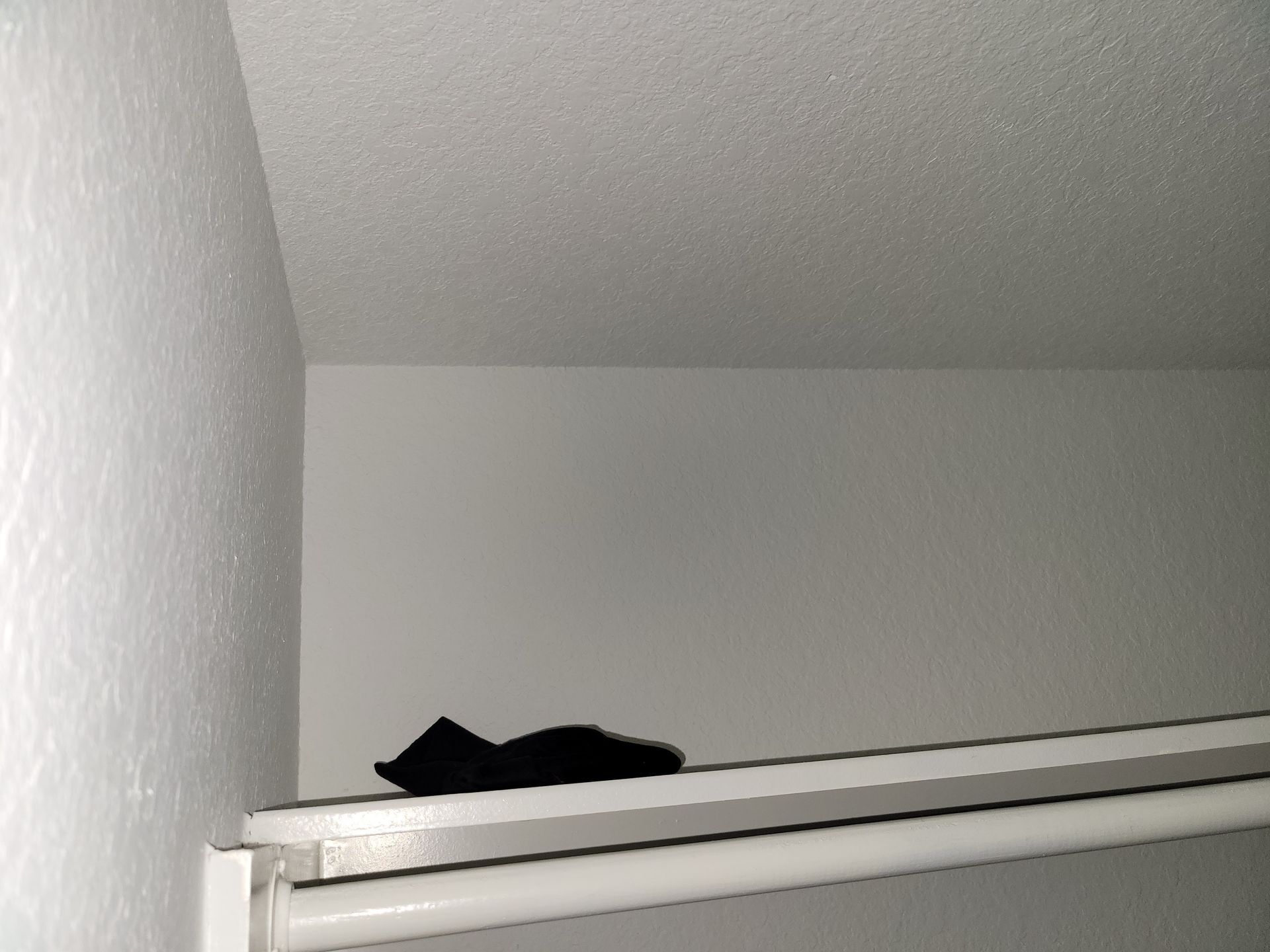 Black item on a white shelf inside a white closet.