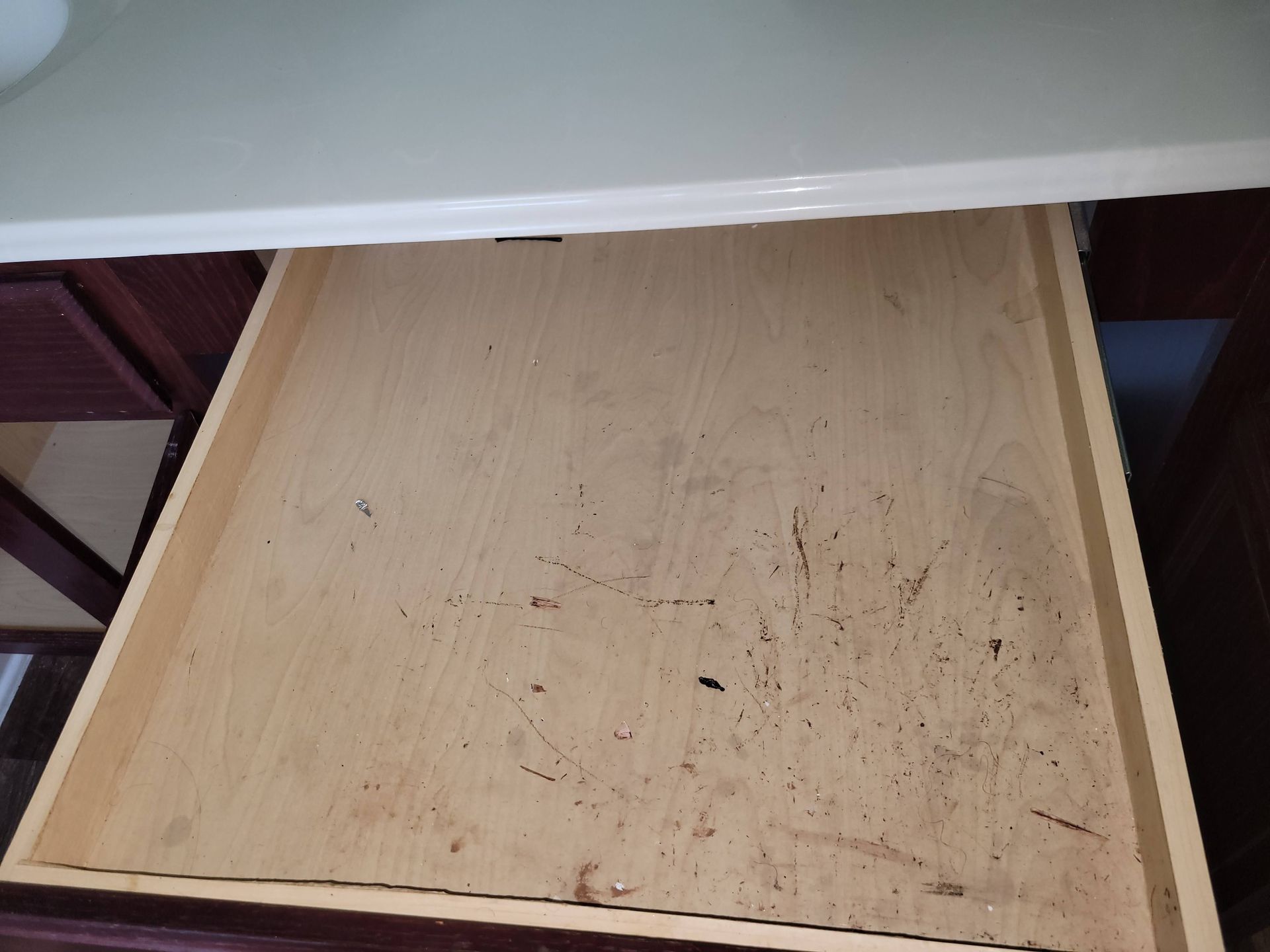 Open, empty wooden drawer inside a dark cabinet.