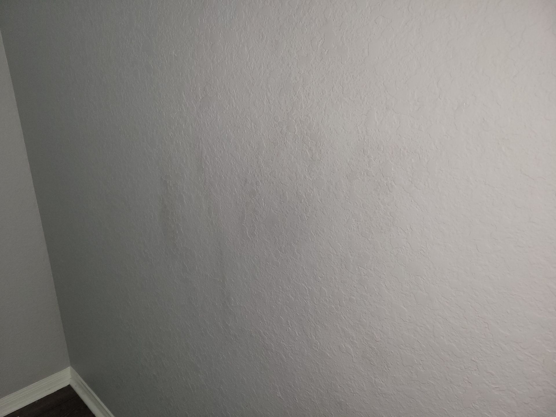 Gray textured wall in a corner of a room, with dark wood flooring.