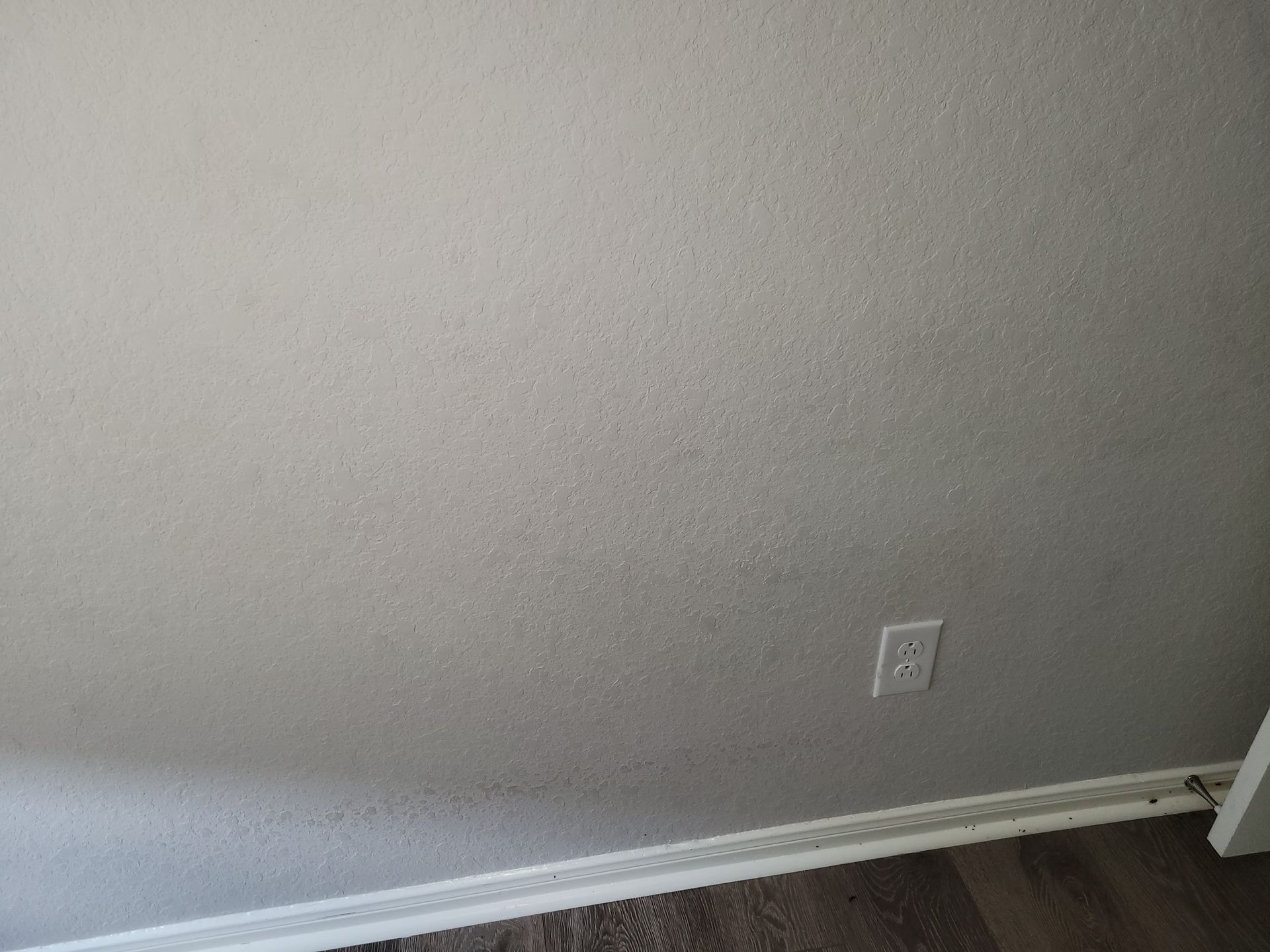 Gray textured wall with an electrical outlet and white baseboard trim.