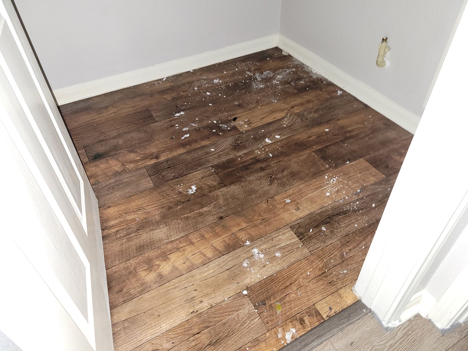 Wooden floor in a small room, covered in white debris, with white trim and gray walls.