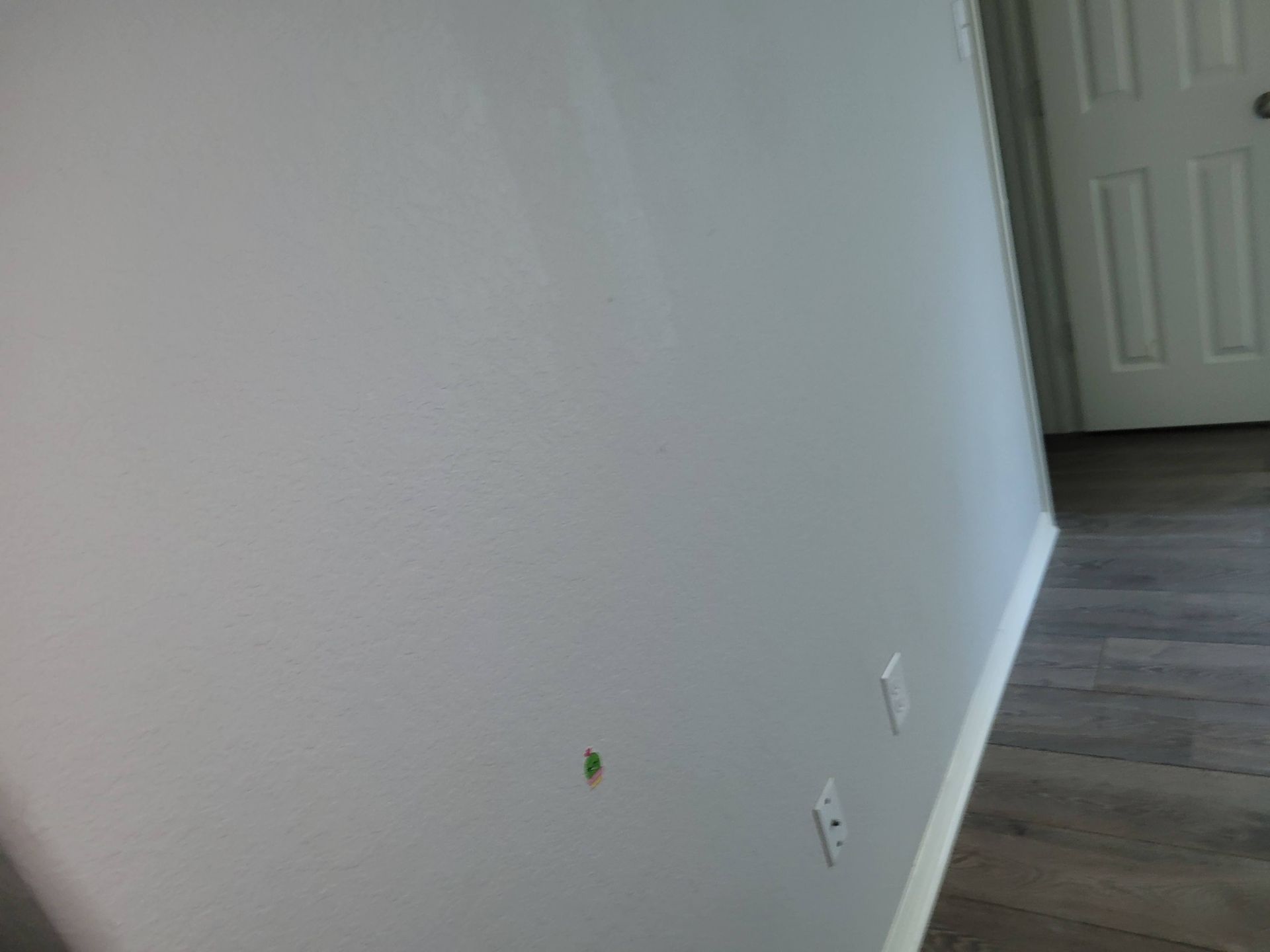 White walls with two electrical outlets and a wooden floor. A closed white door is on the right.