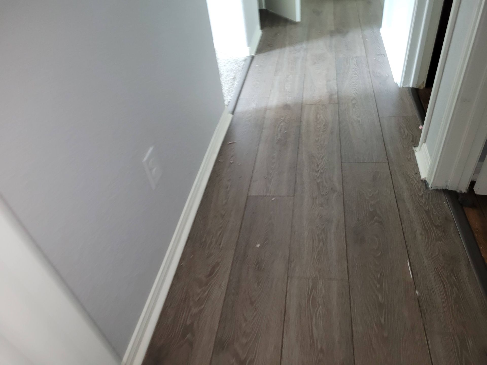 Narrow hallway with gray wood-look flooring and light gray walls, leading to doorways.