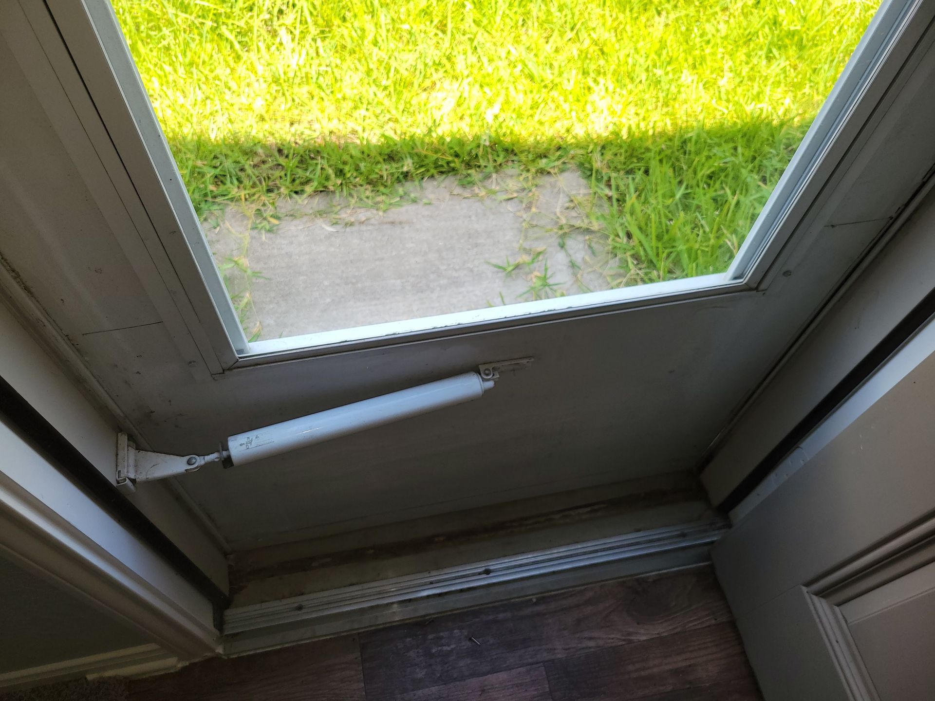 Open white door with a screen, showing green grass and a door closer.