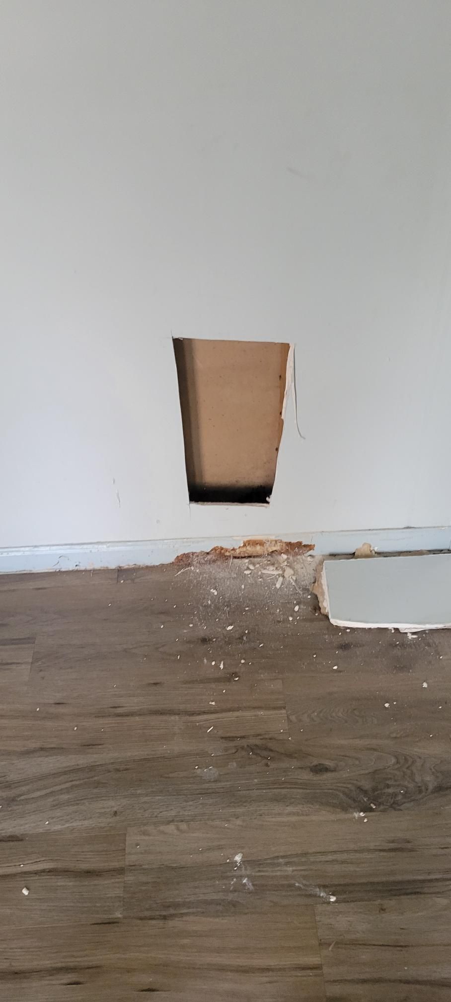 Hole cut in a wall above a wood floor with debris.