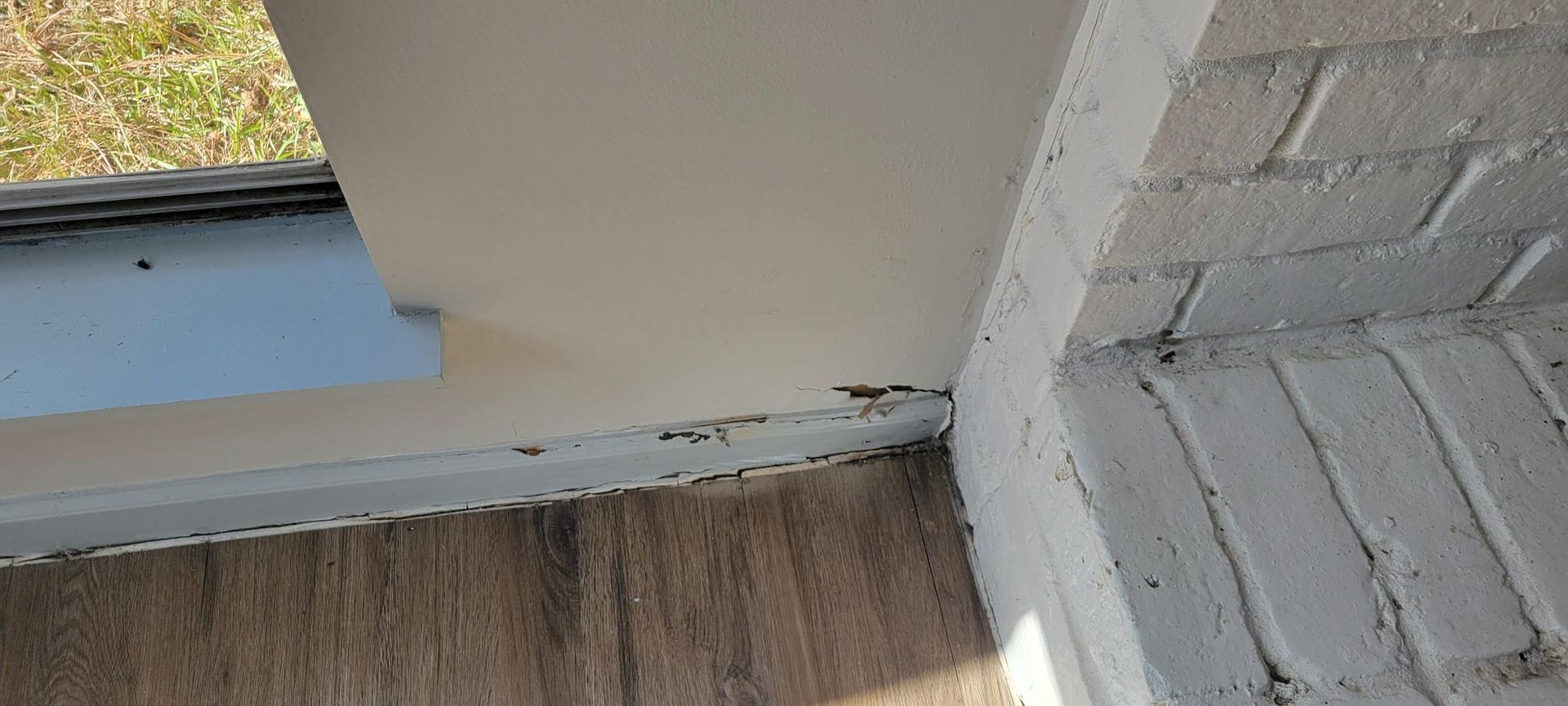 Corner of a building with painted brick and interior trim next to what appears to be a window.