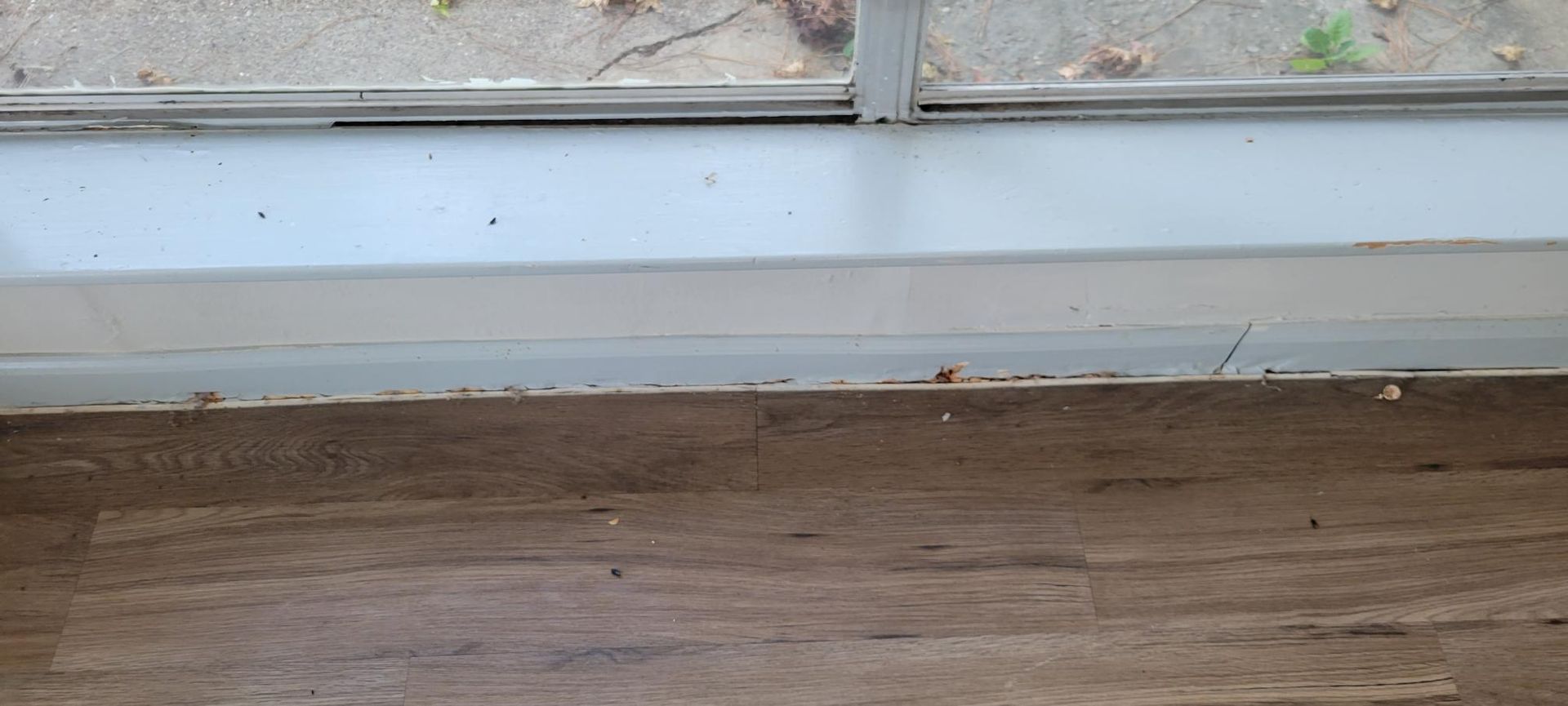 Wooden floor meeting a white window frame, showing the edge of the window and the floorboards.