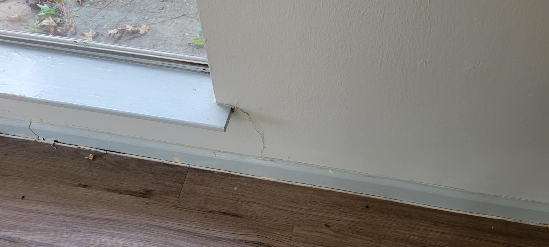 Close-up of a white painted wall and window frame with a wooden floor.