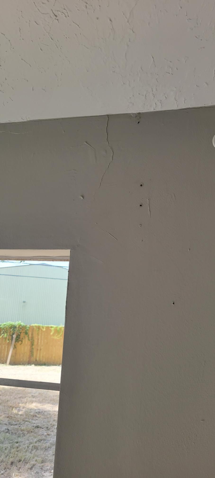 A grey wall with small marks and a window opening to greenery outside. The ceiling is white.