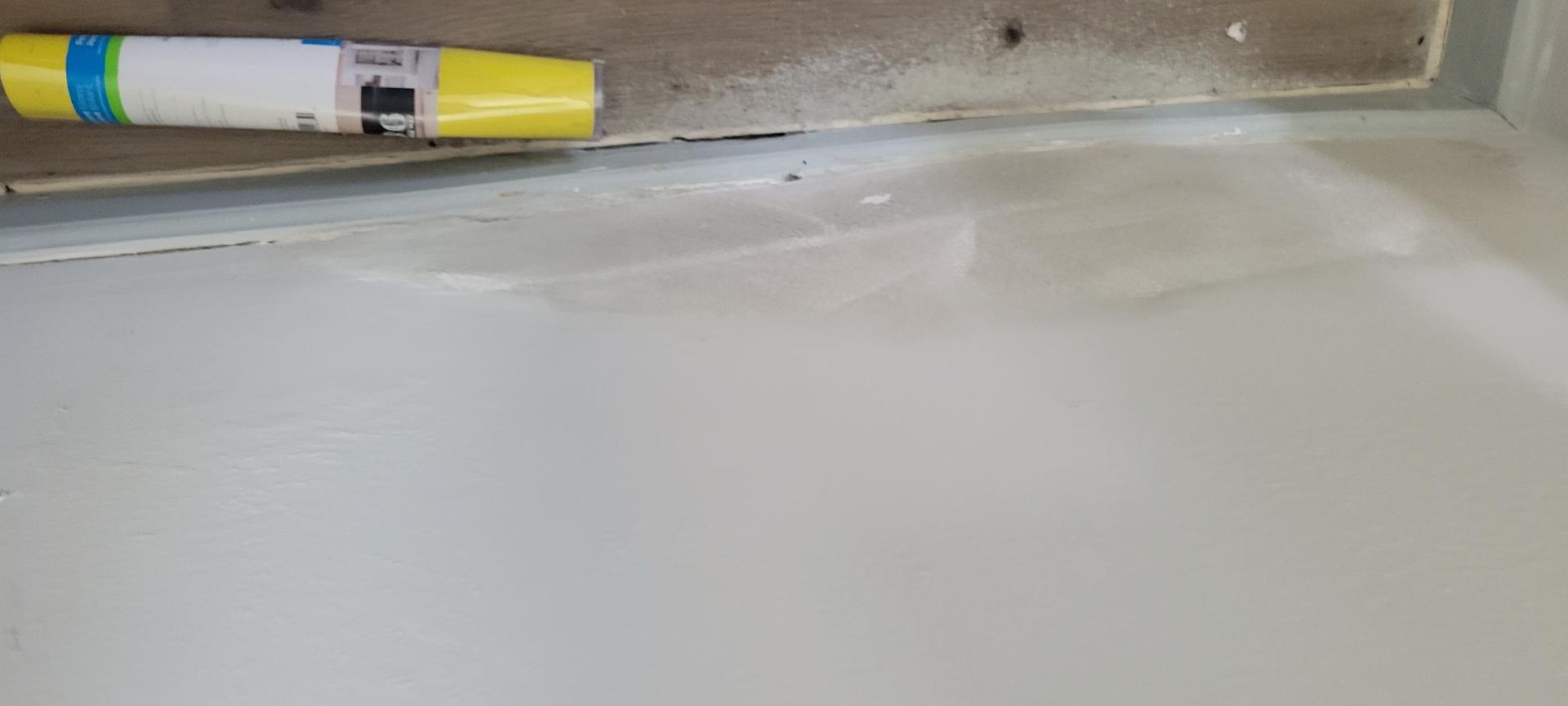 A white painted surface with a yellow object. A light tan wall is above the white surface.