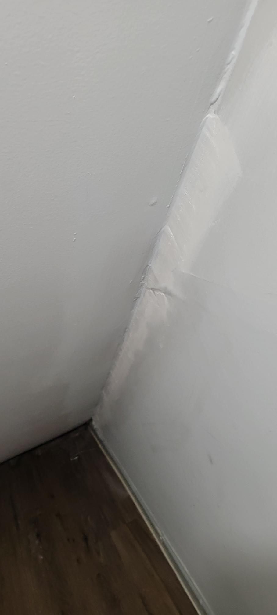 White walls meeting at a corner. Light colored flooring. There is visible cracking in the wall.