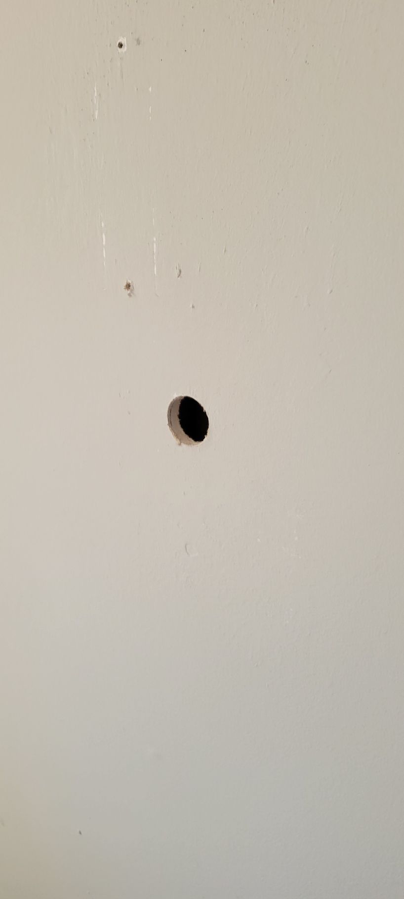 A hole in a beige wall, with a dark interior and small specks nearby.